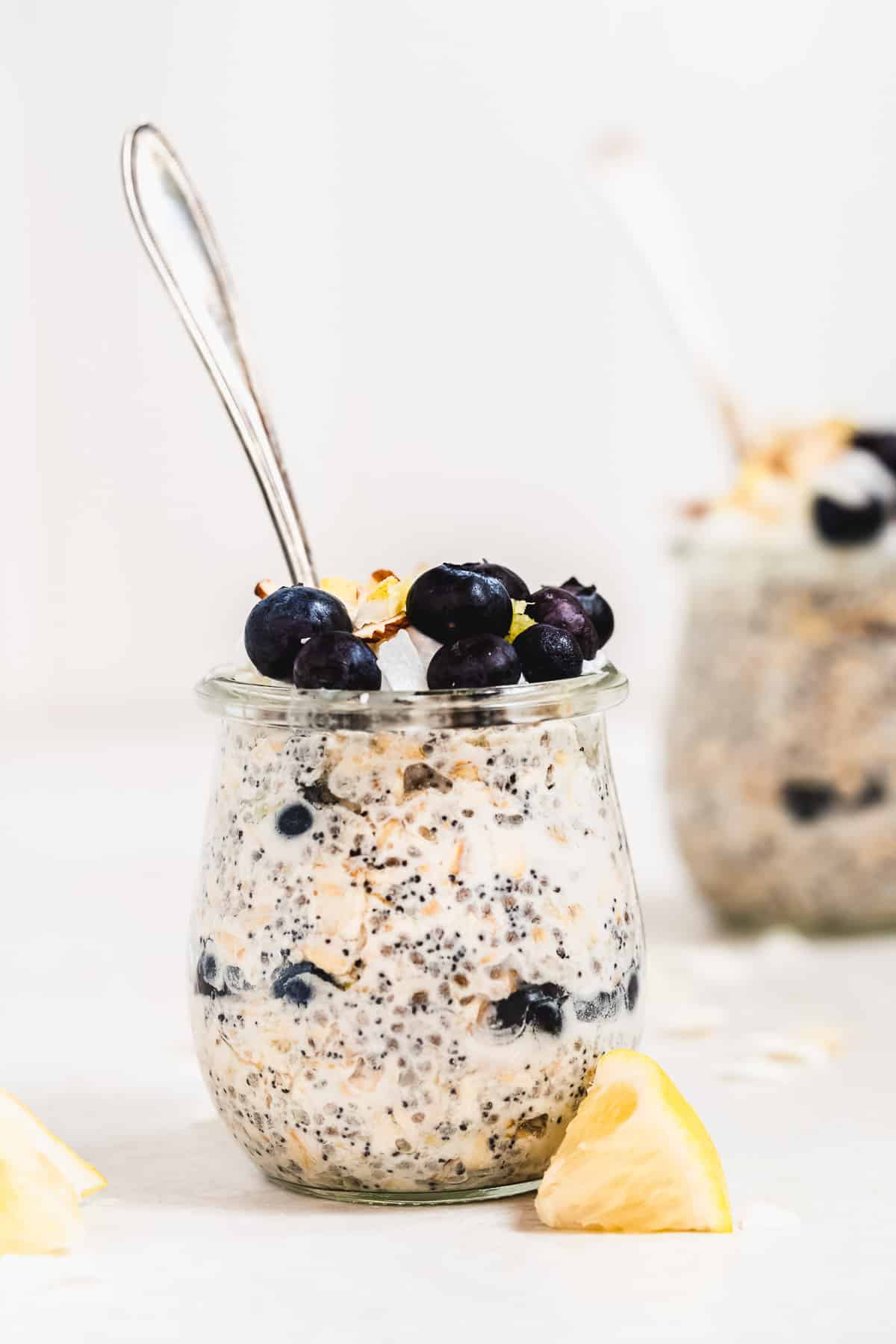 Jar full of oats with blueberries on top and spoon on a white surface.