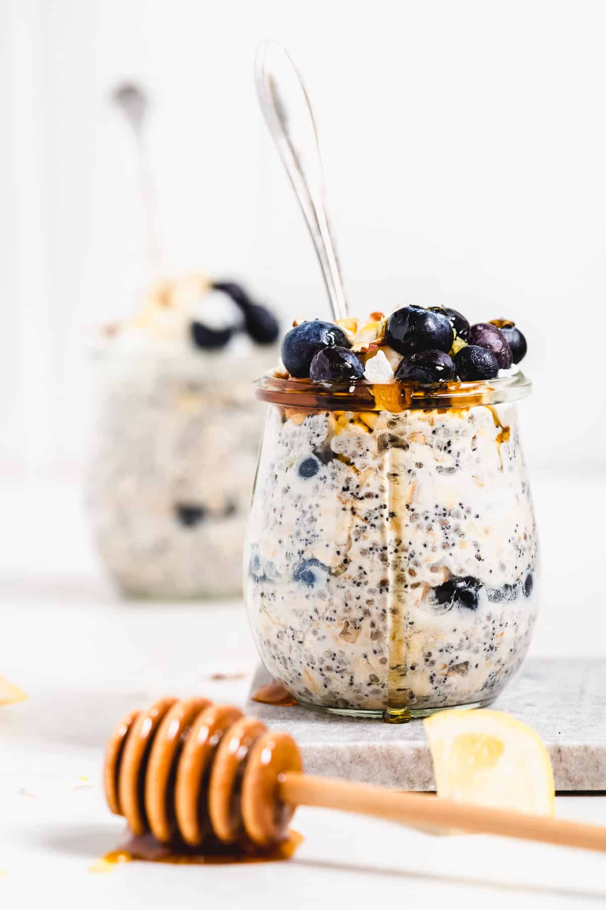 Glass full of oats with blueberries on top and honey dripping down the sides.