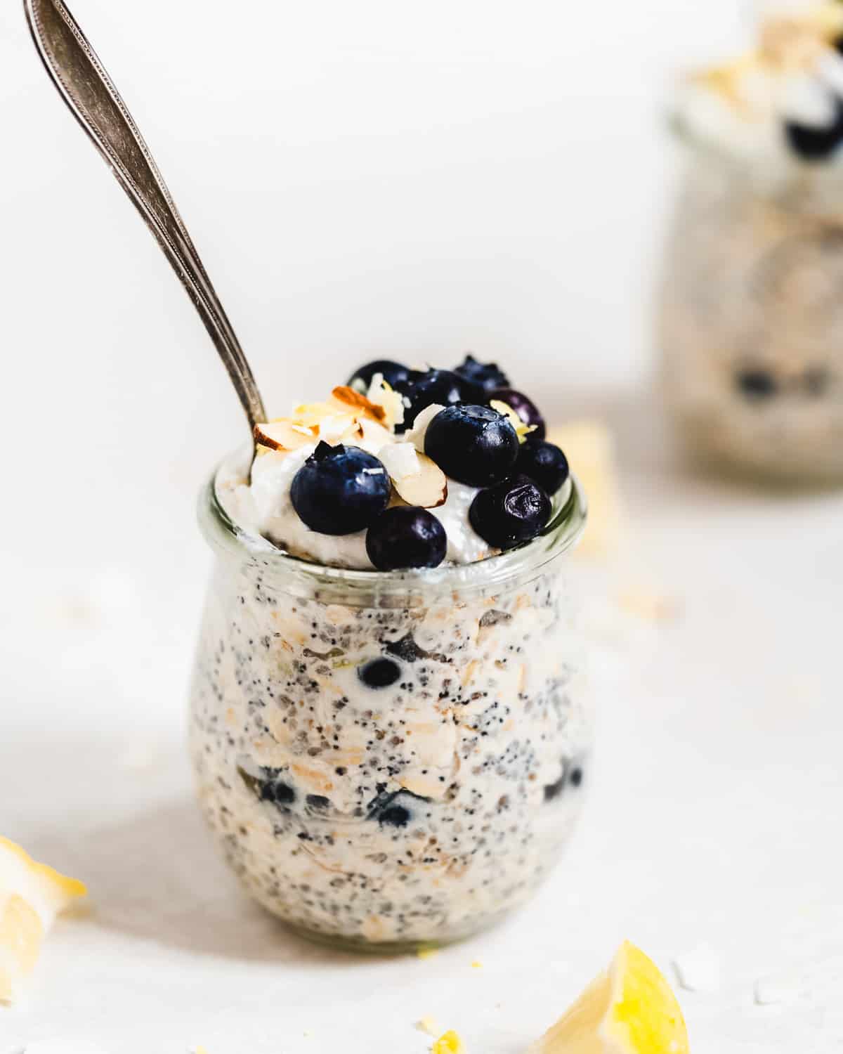 Jar full of oats with blueberries on top and a spoon inside.