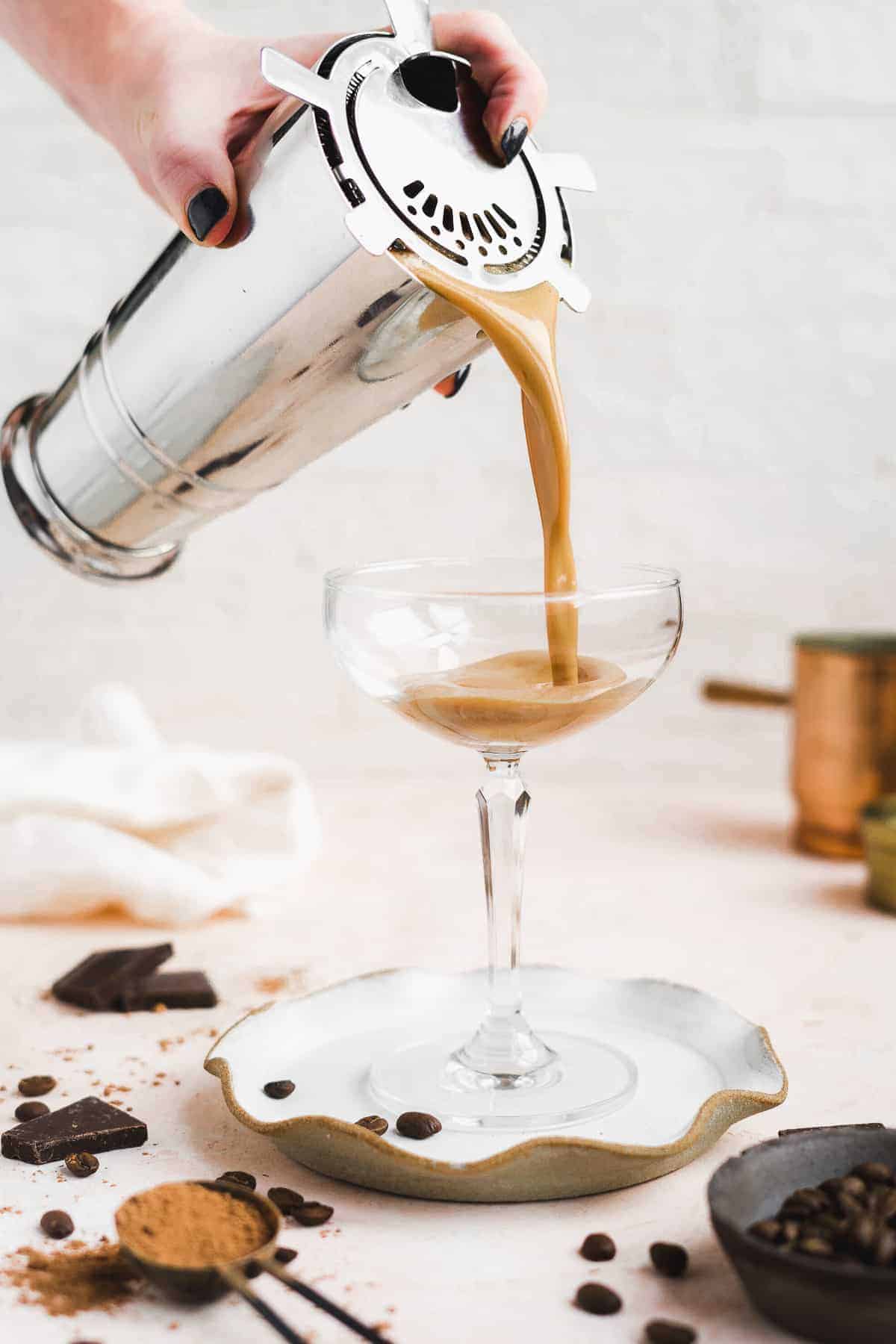 Person pouring martini into a glass on a plate.