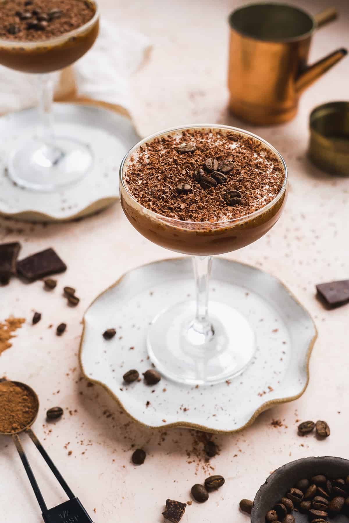 Glass filled with chocolate cocktail on a plate on a pink surface.