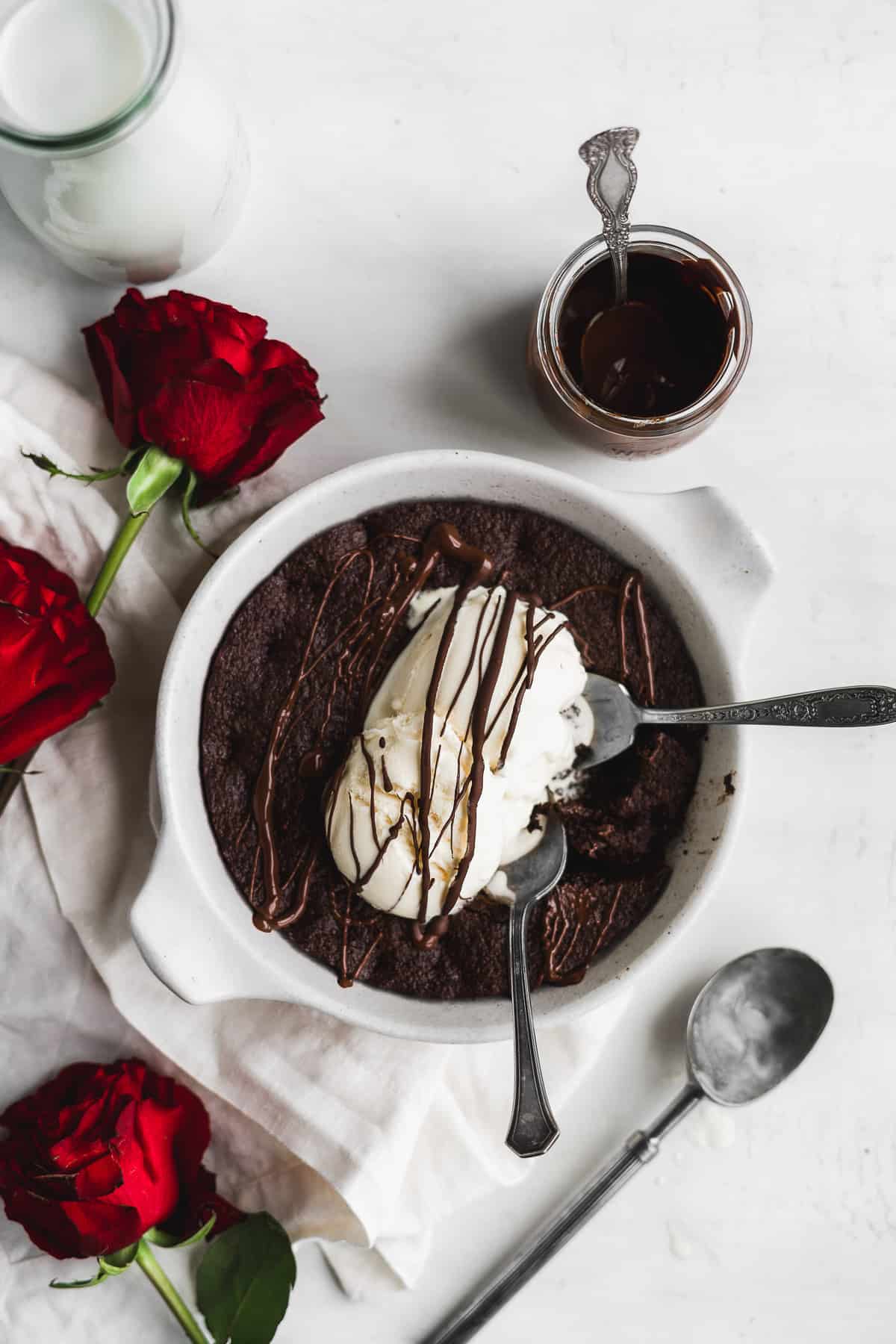 Chocolate brownie in a white skillet with ice cream on top and roses on the side.