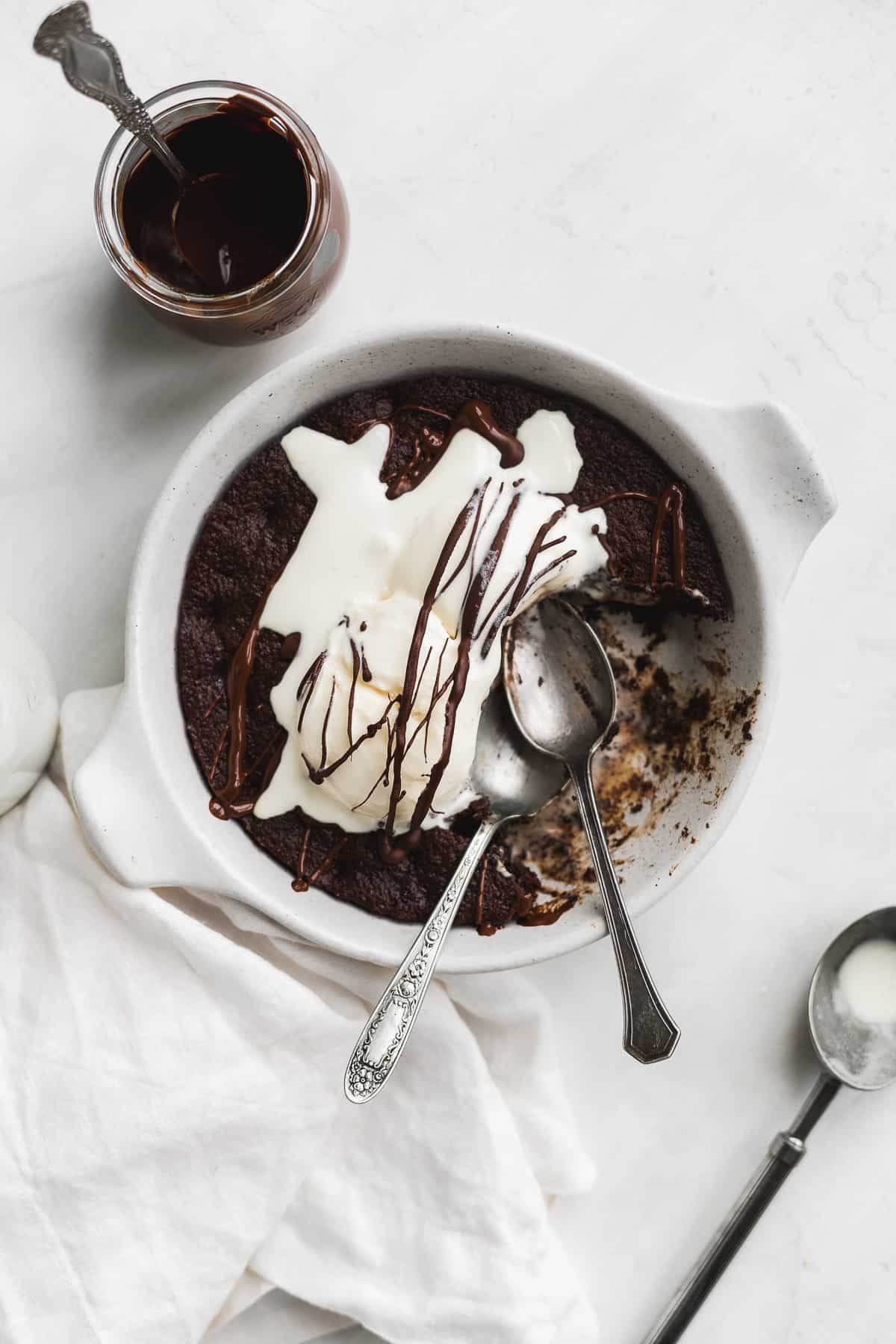 White skillet with brownie and ice cream and two spoons with a piece missing.