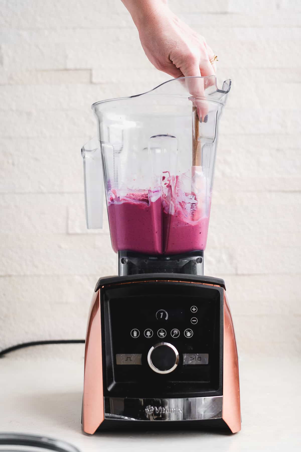 Pink smoothie in blender with hand scraping down the sides.
