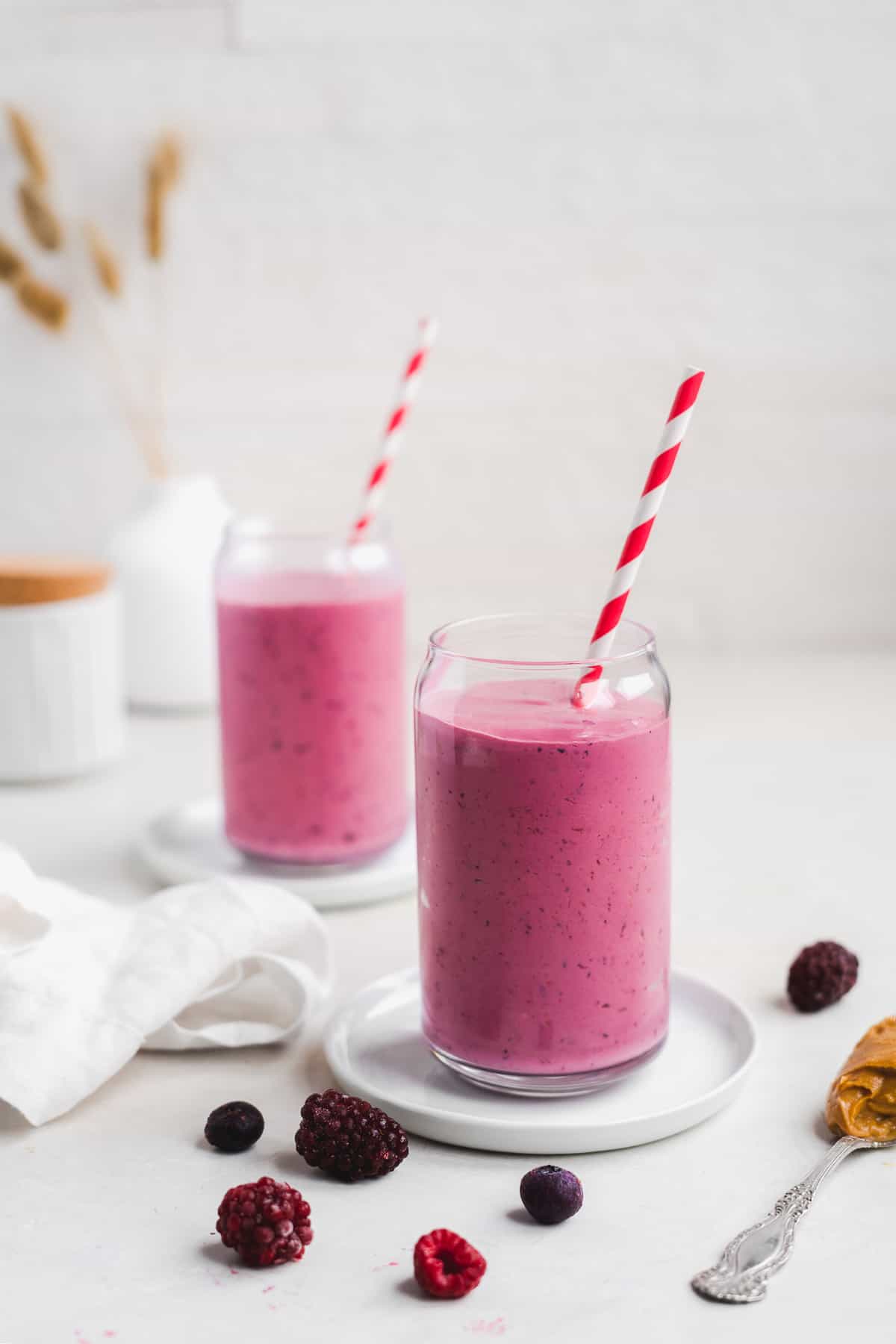 Glass full of pink smoothie with red and white straw on a white surface.