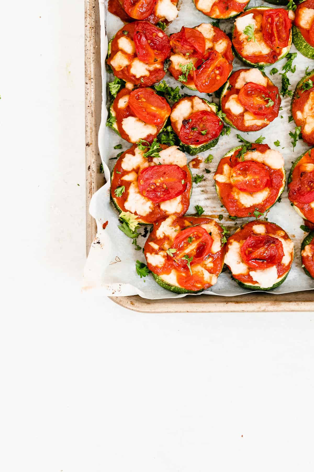 Baking sheet filled with zucchini topped with cheese and tomato sauce.