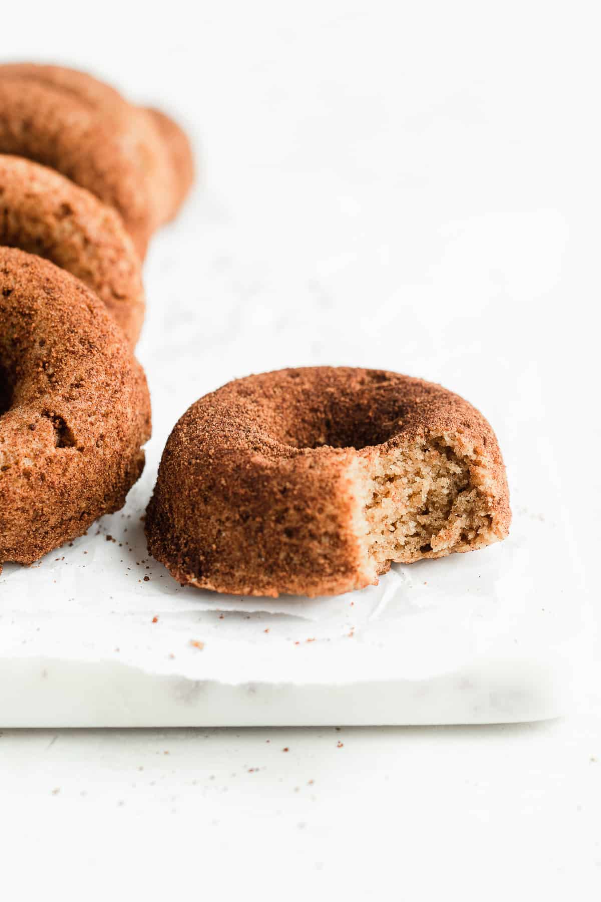 Cinnamon doughnut on a marble plate with a bite taken out of it.