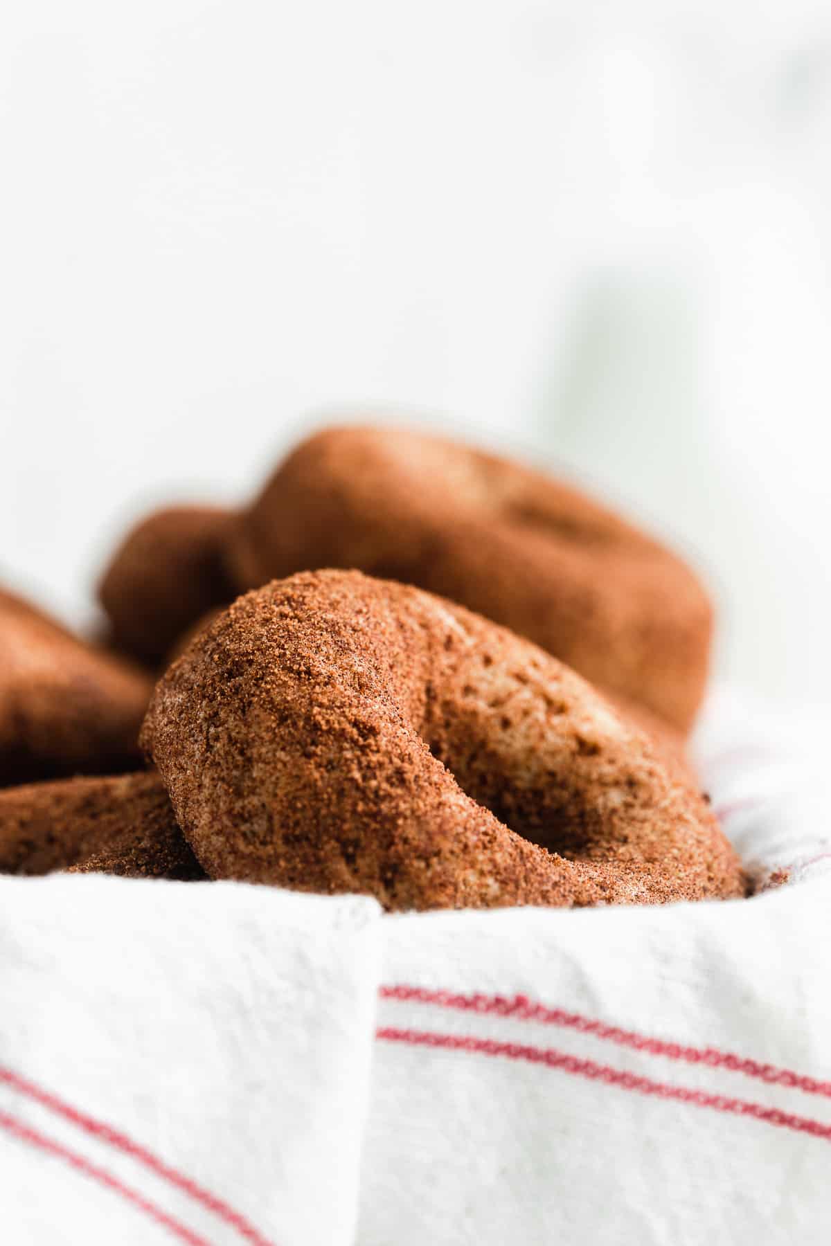 Cinnamon doughnuts in a basket with a white and red cloth.