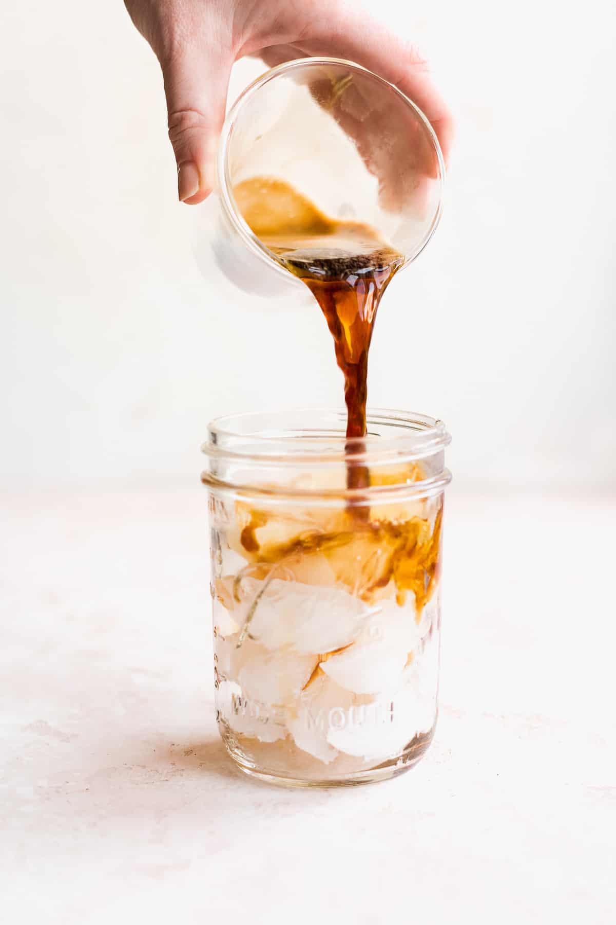 Hand pouring coffee into a glass with ice.