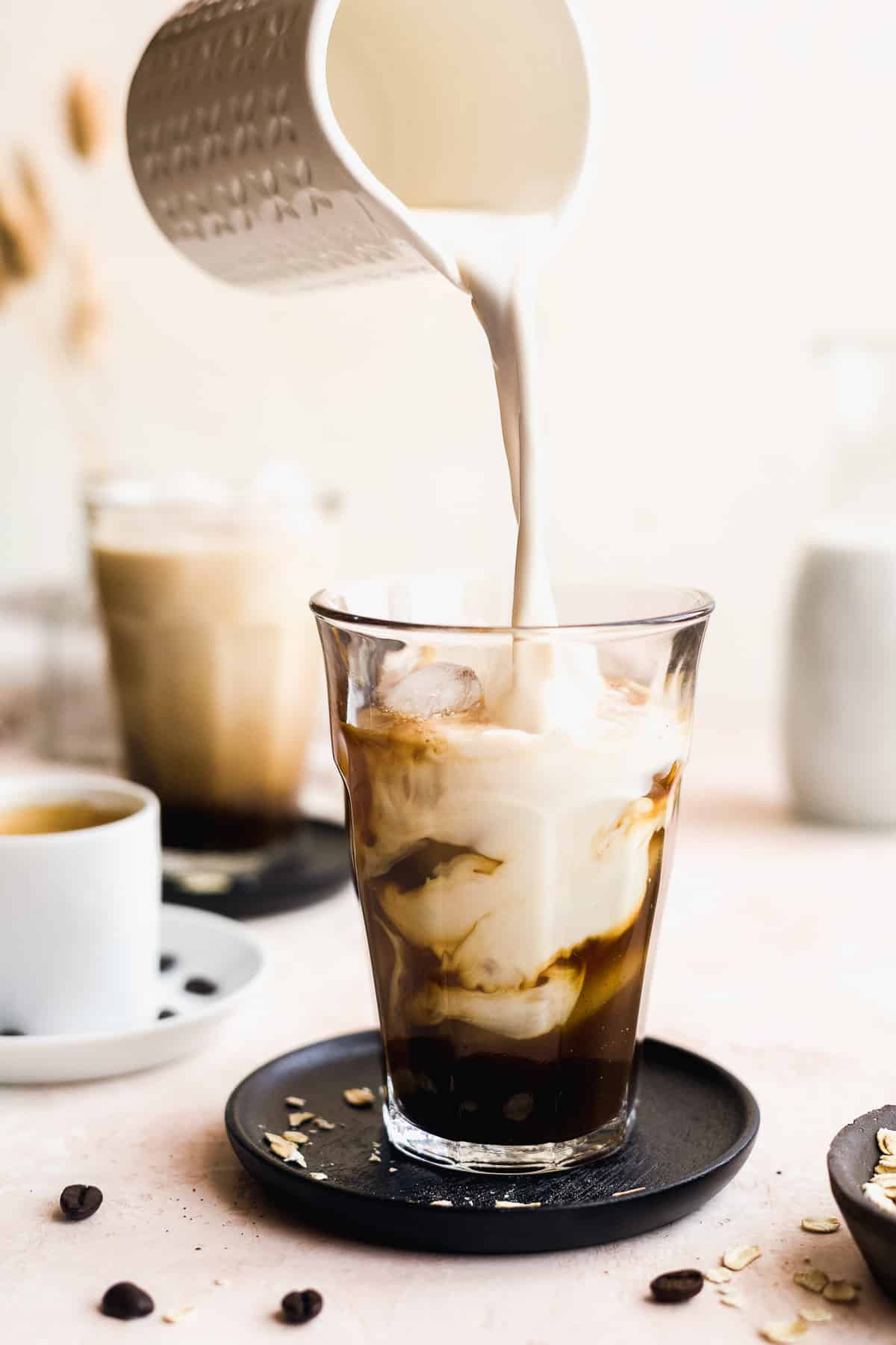 Milk bring poured into glass with iced coffee on a black coaster.