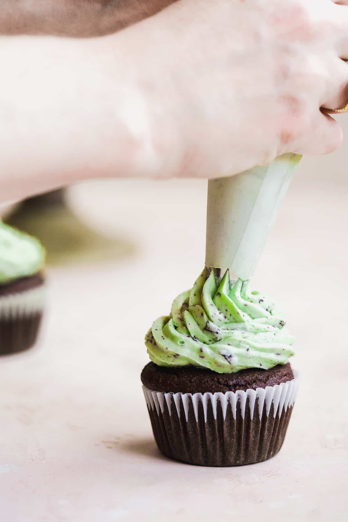 Hand icing green frosting on top of a chocolate cupcake.