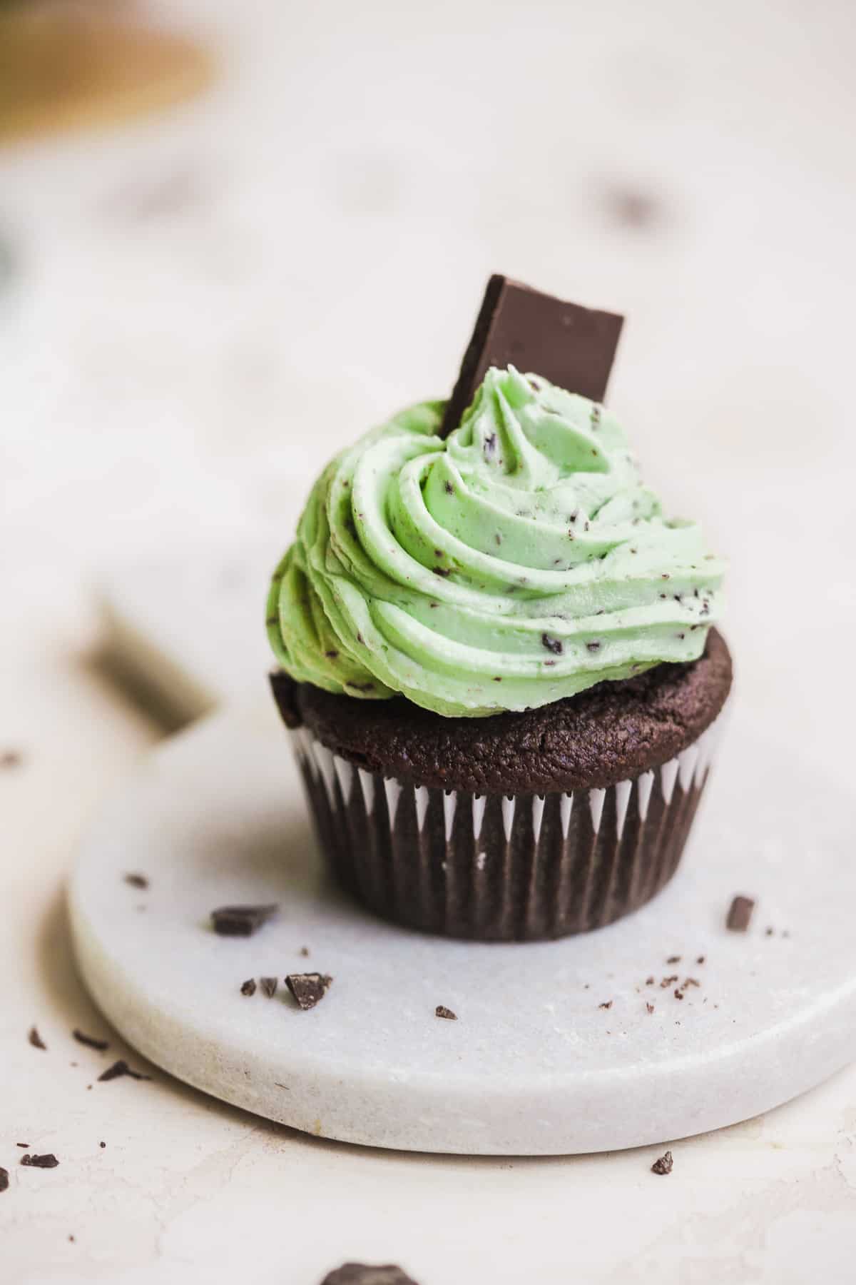 Chocolate cupcake with green icing on a marble circle with chocolate on top.