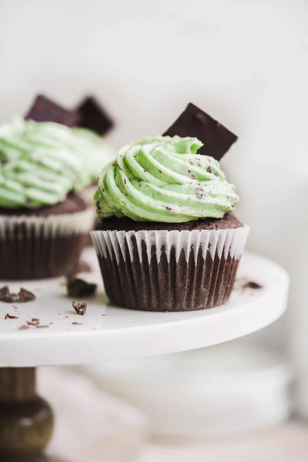 Chocolate cupcake with mint green icing on a white marble cake stand with chocolate on the surface.