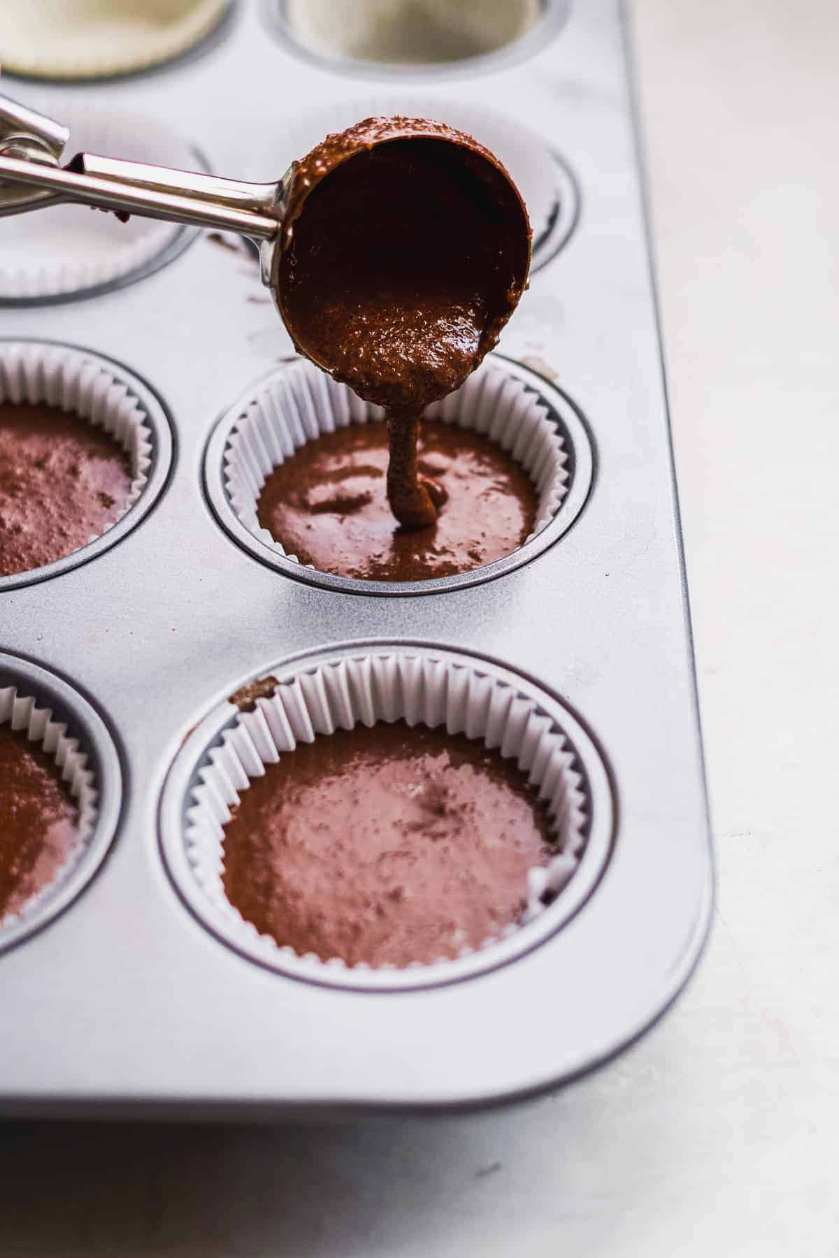 Cookie scoop pouring chocolate batter into cupcake liners.