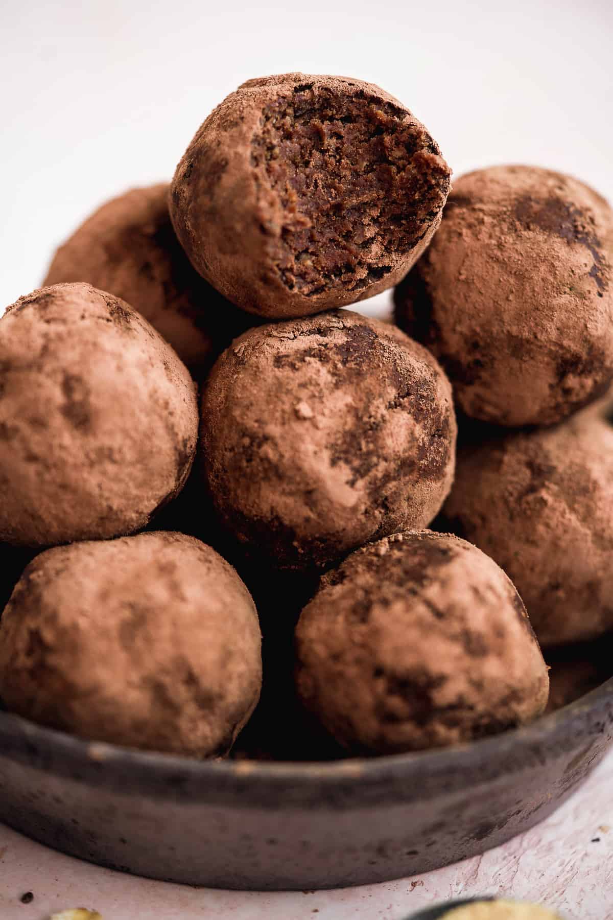 Chocolate protein balls stacked in a container on top of one another with a bite taken out of the top one.
