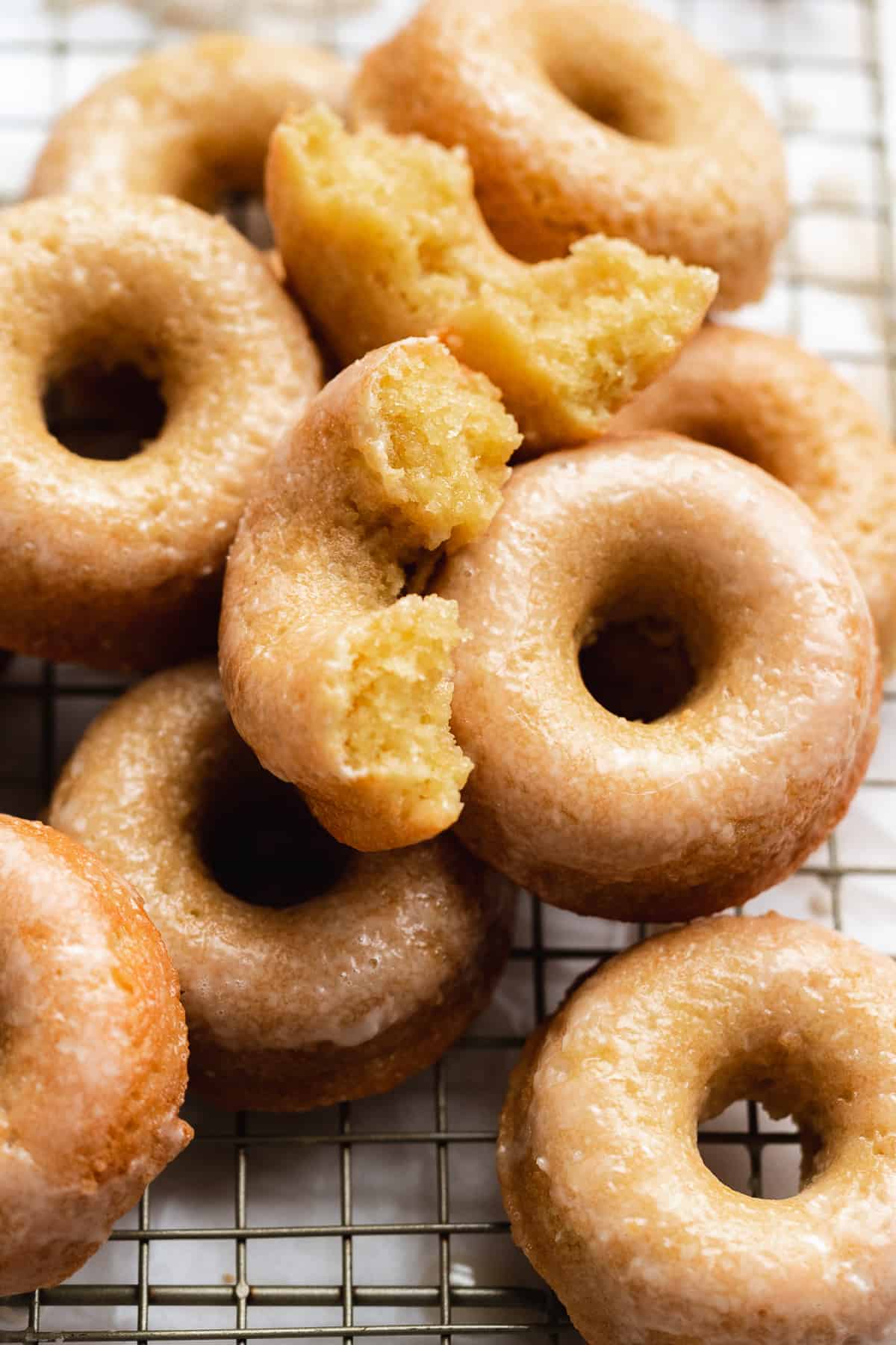 Glazed donuts scattered on a wire rack with one broke in half.