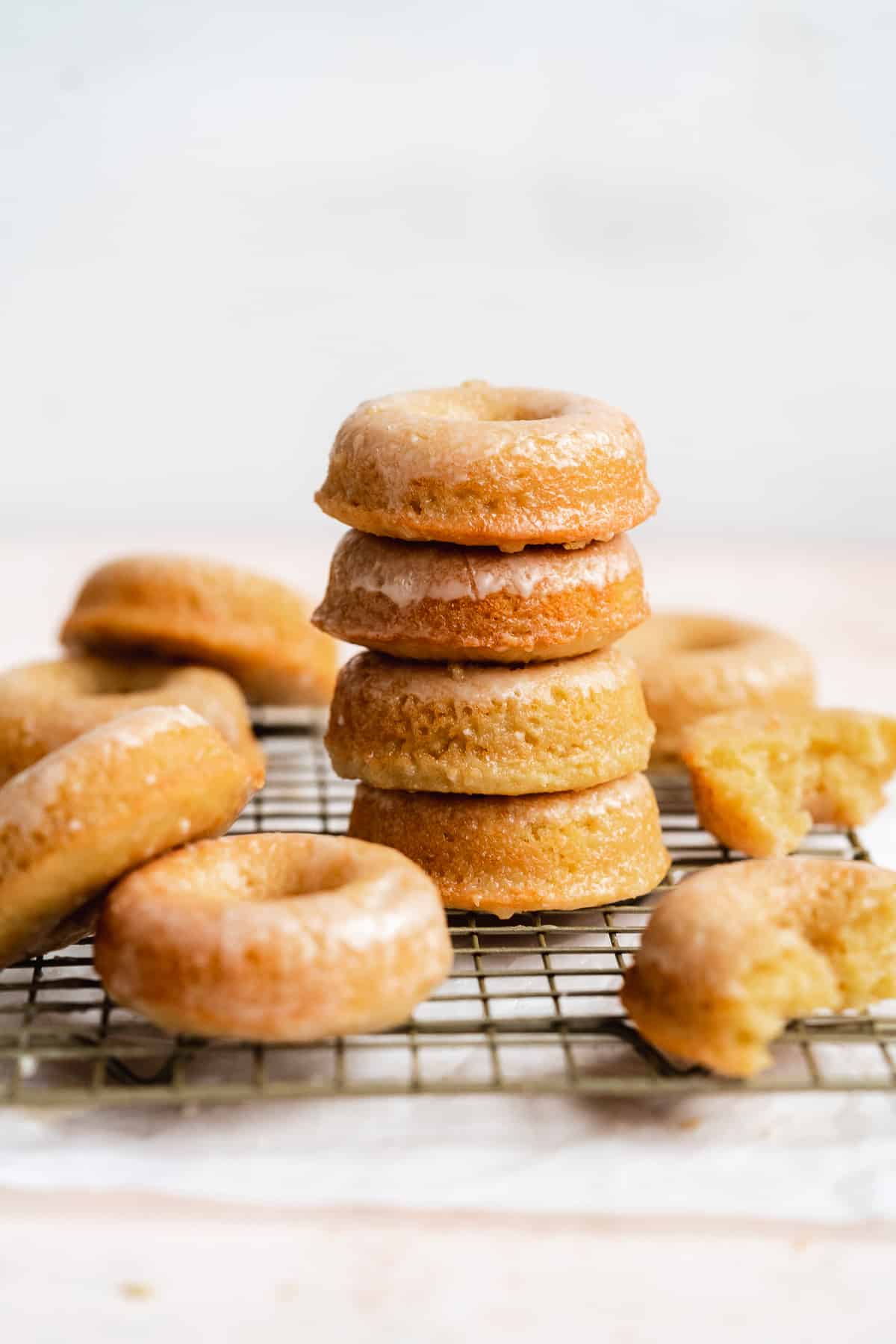 Glazed donuts stacked on a wire rack with donuts scattered on surface.
