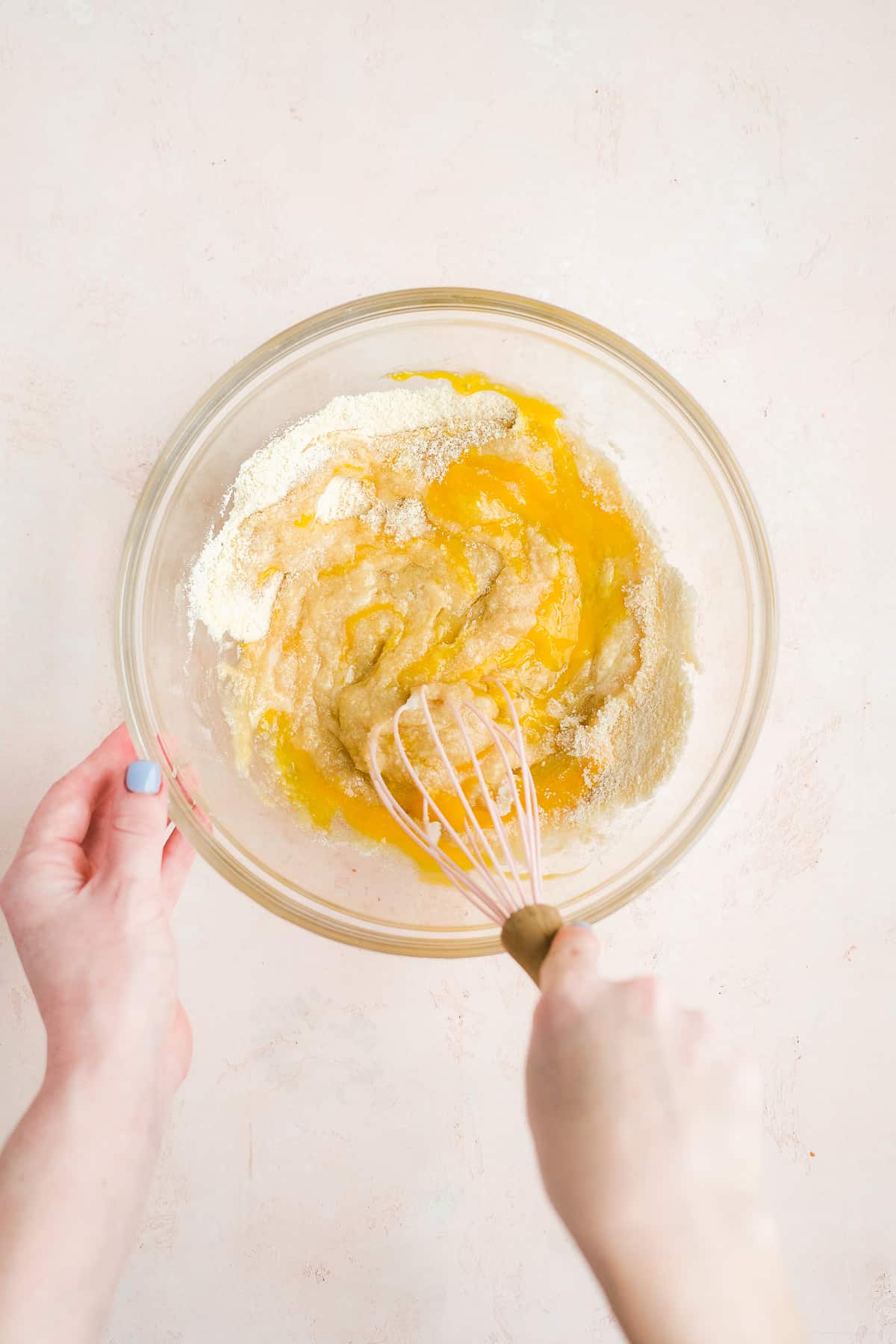 Person whisking together gluten free donut batter in a glass bowl.