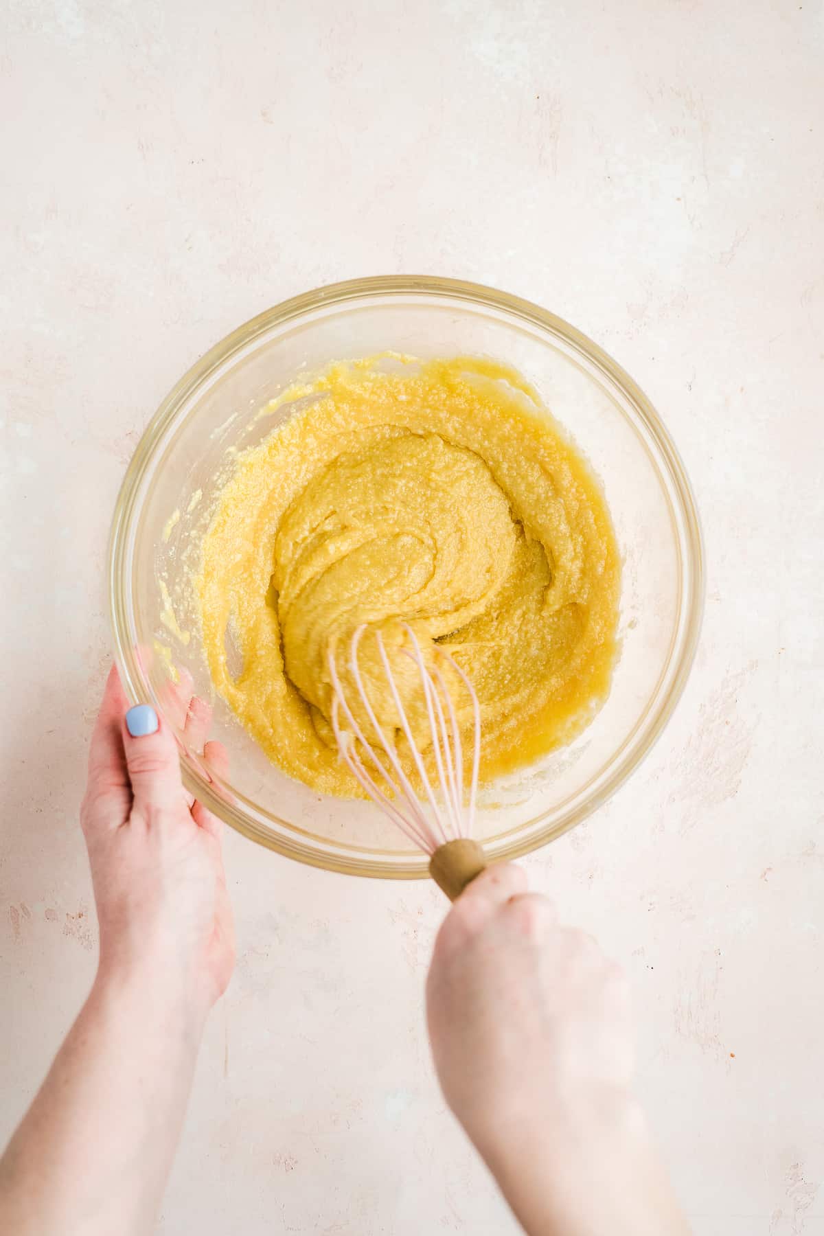 Hand mixing batter in a mixing bowl with a whisk.