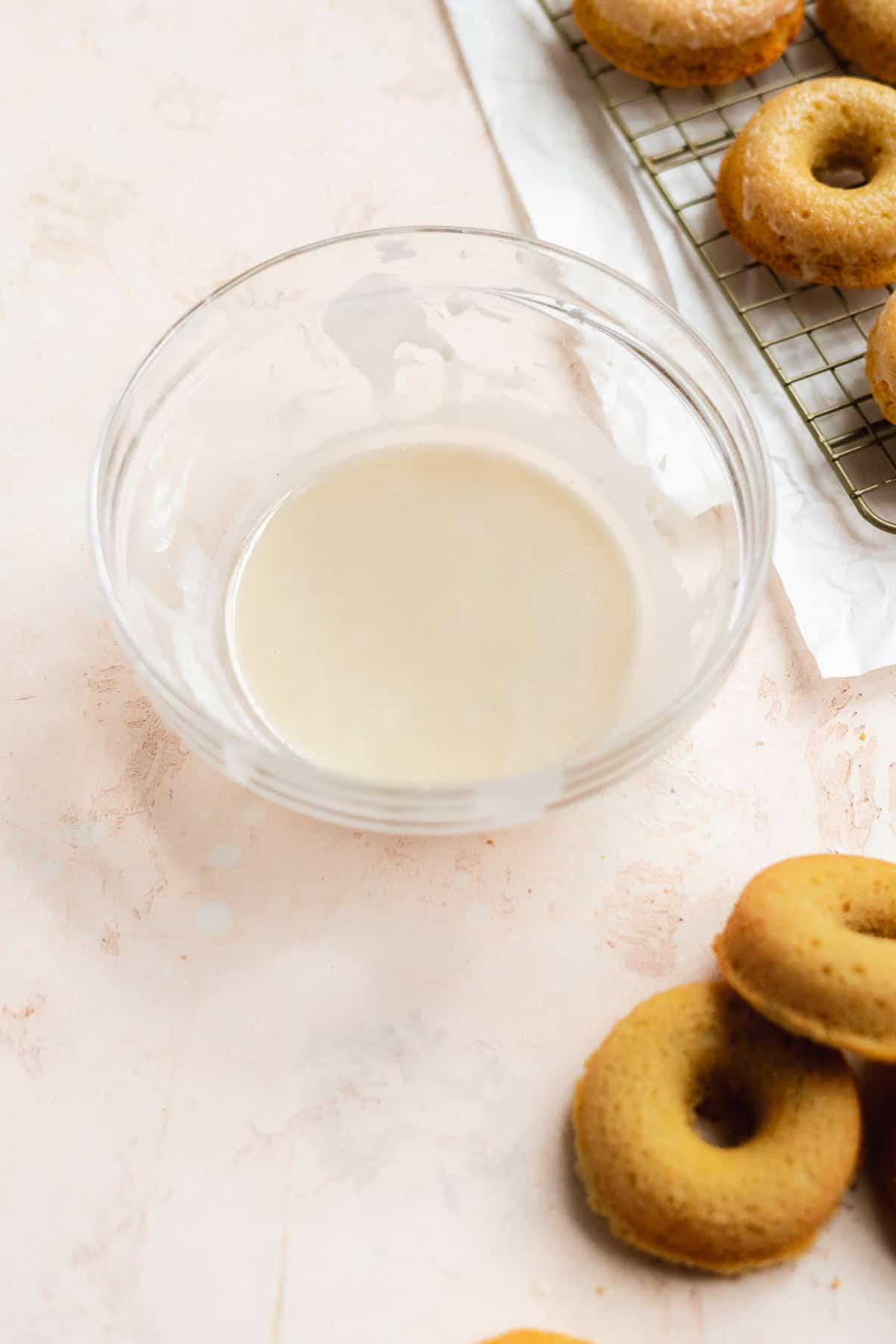 Glass bowl with vanilla glaze inside and donuts on the side.