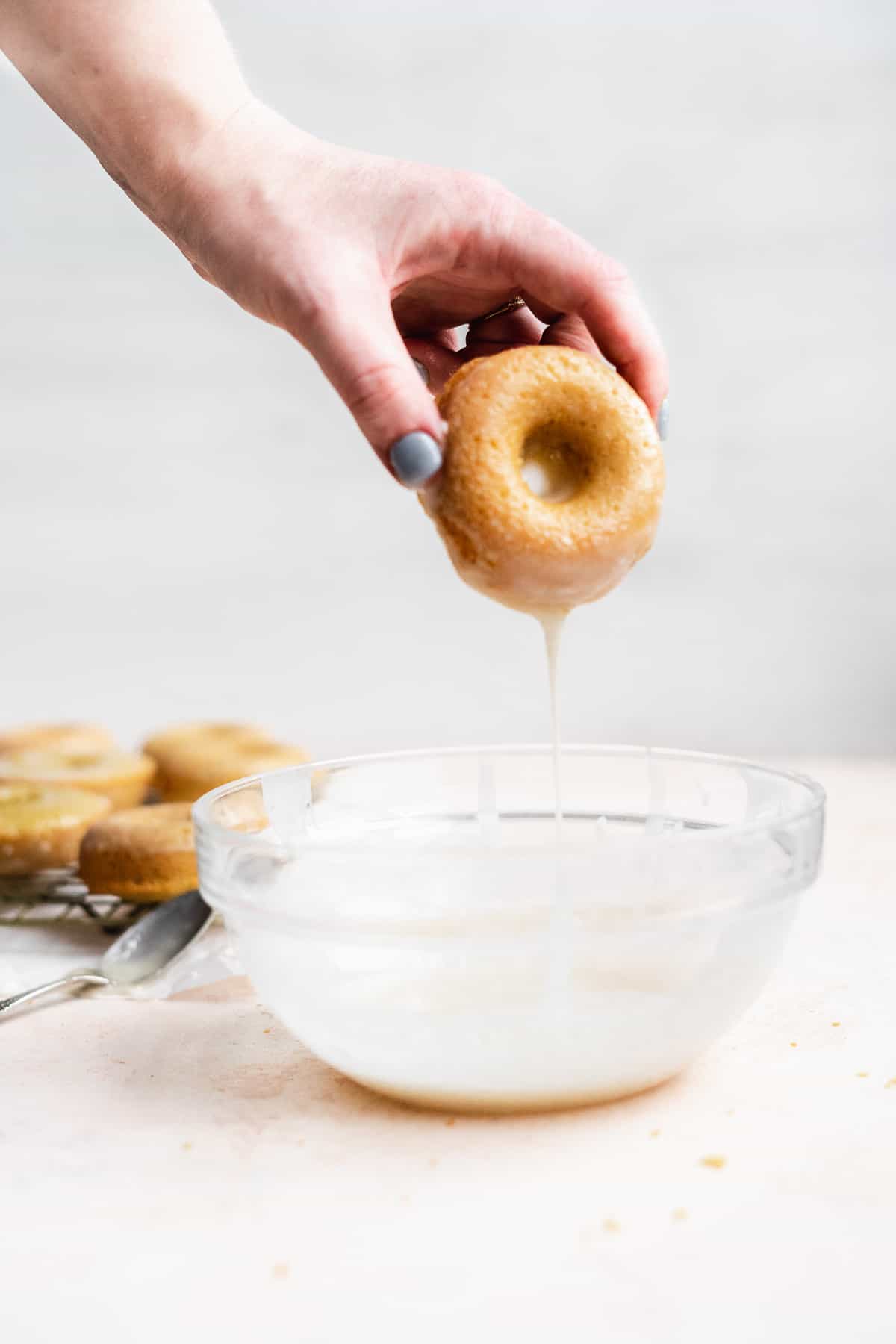 Hand dipping donut in vanilla glaze and letting it drip off.