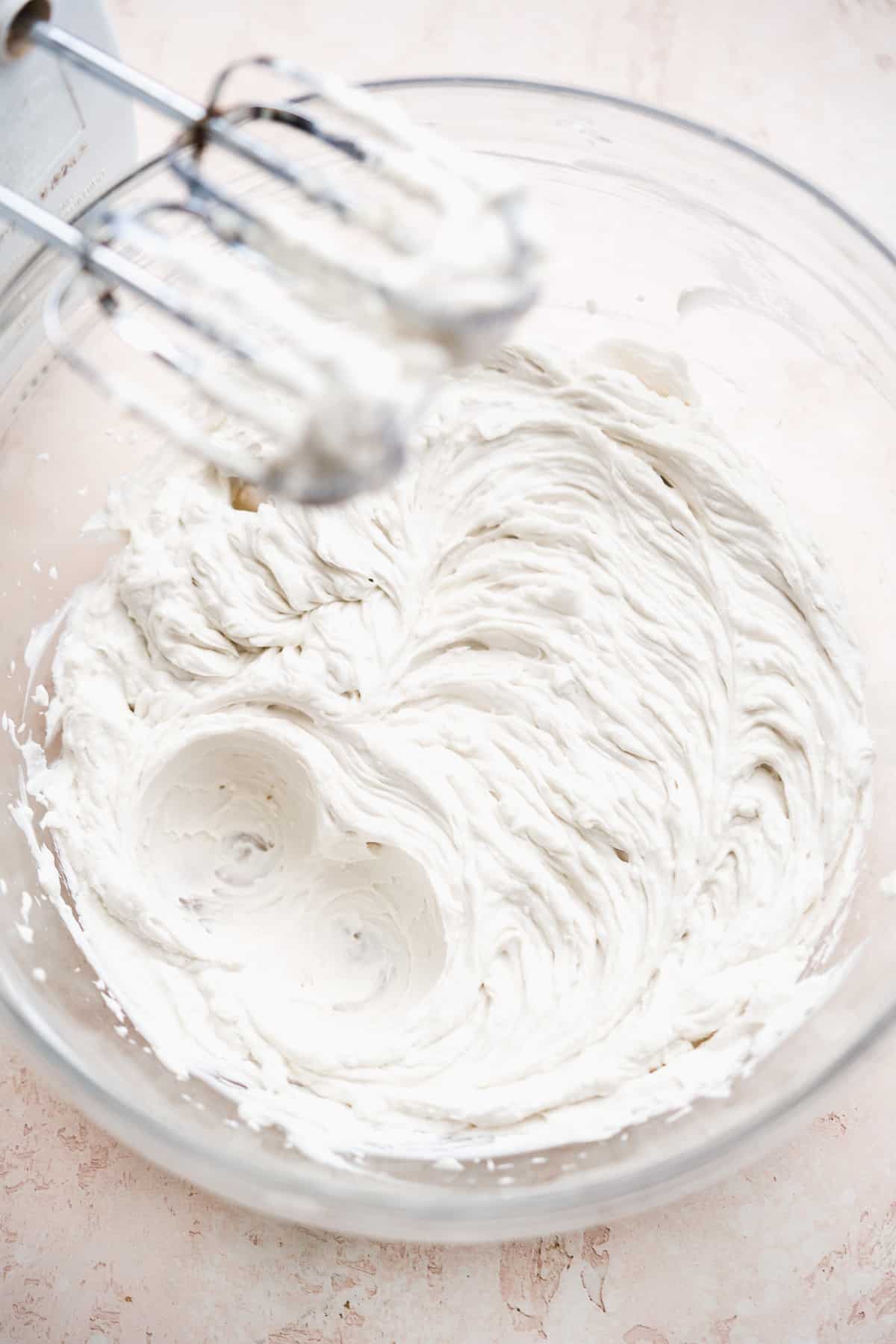 Bowl full of whipped coconut cream with hand mixer.