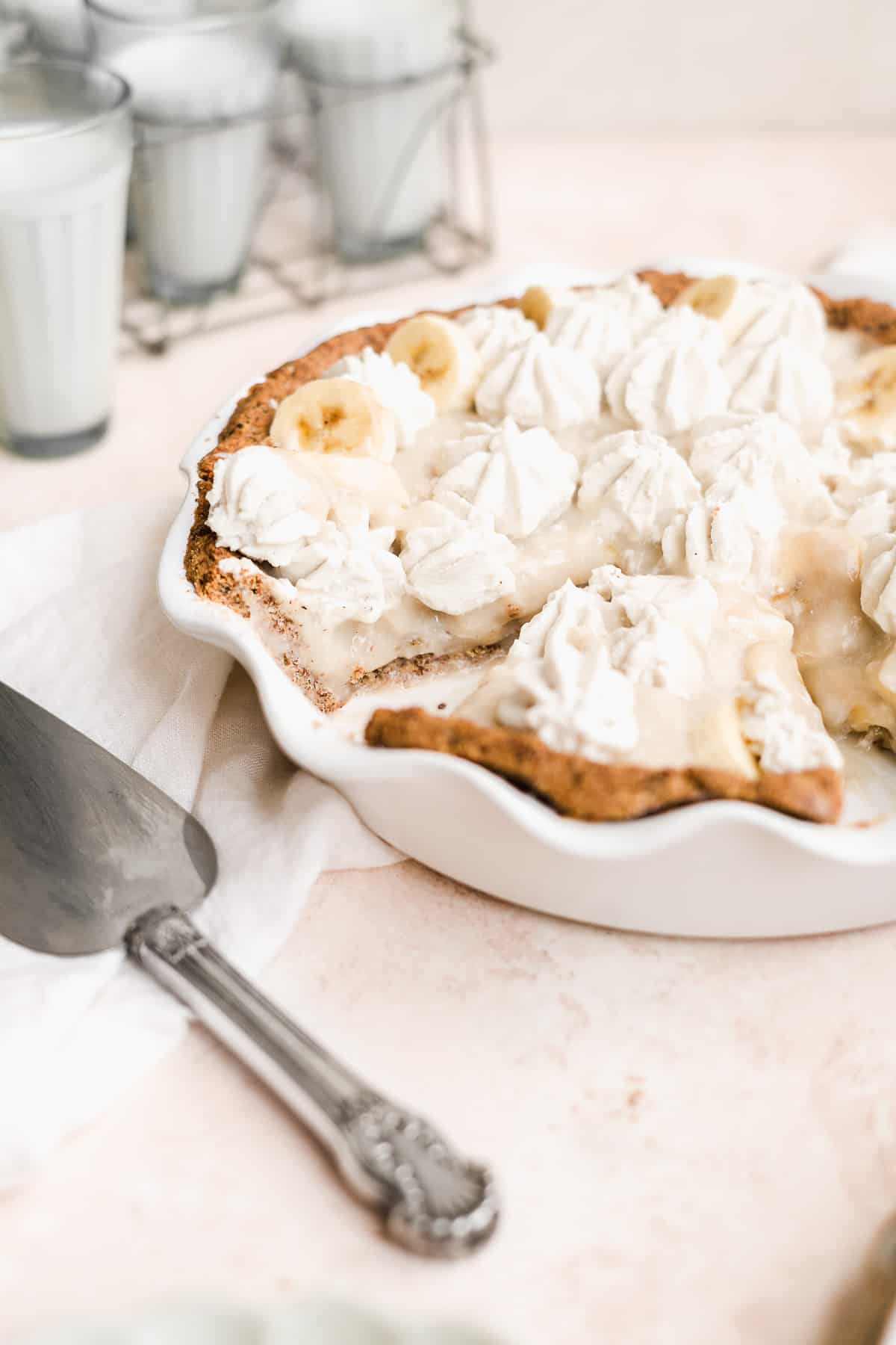 Side view of banana pie with whipped cream on top and a pie cutter in front.