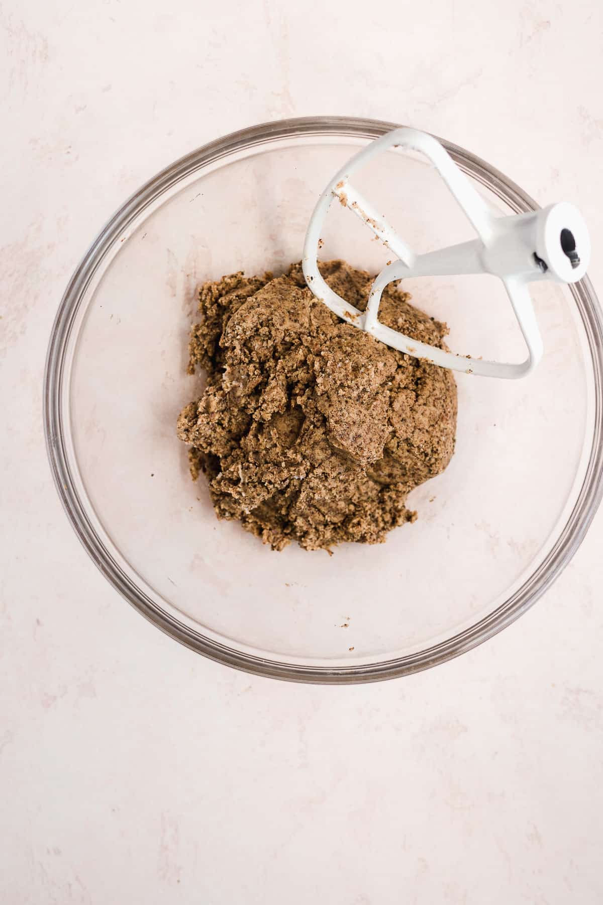 Image of pie dough in a glass bowl with mixer resting in bowl.