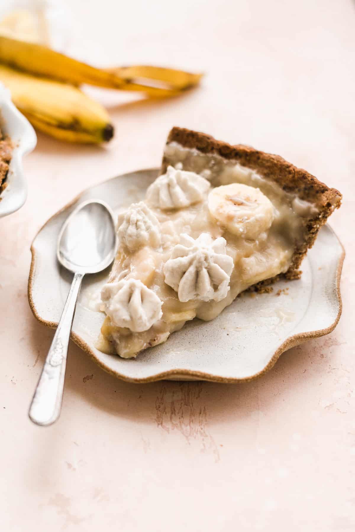 Slice of banana pie on a small ruffle plate with a spoon.