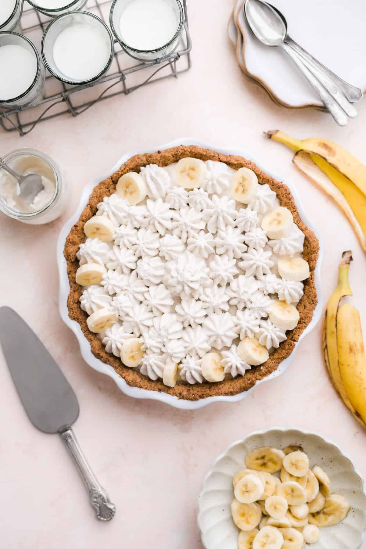 Pie with whipped cream pipped on top on a pink surface with banana peels off to the side.