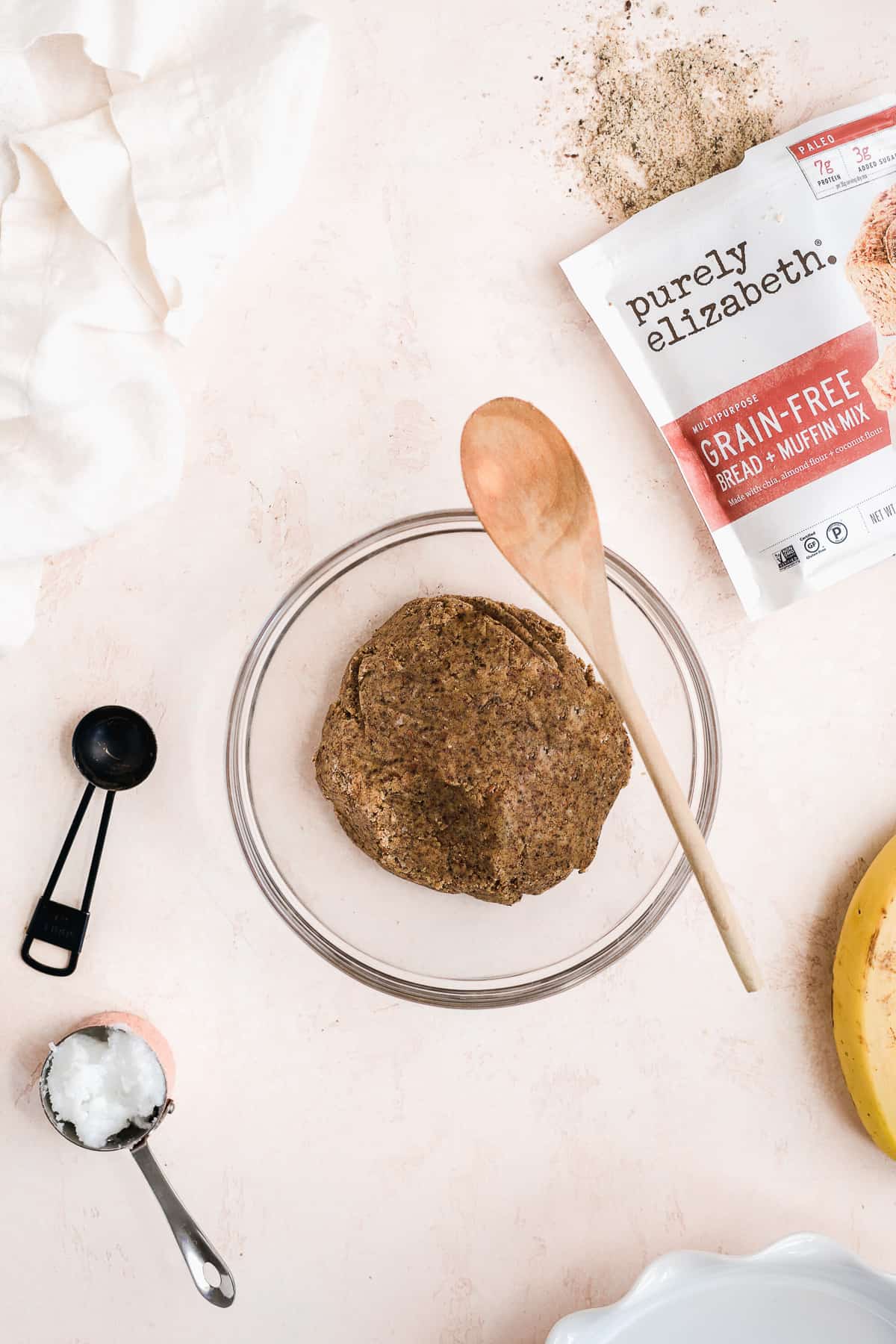 Pie dough in a glass bowl and a wooden spoon resting on bowl with baking mix spilled on the surface to the side.