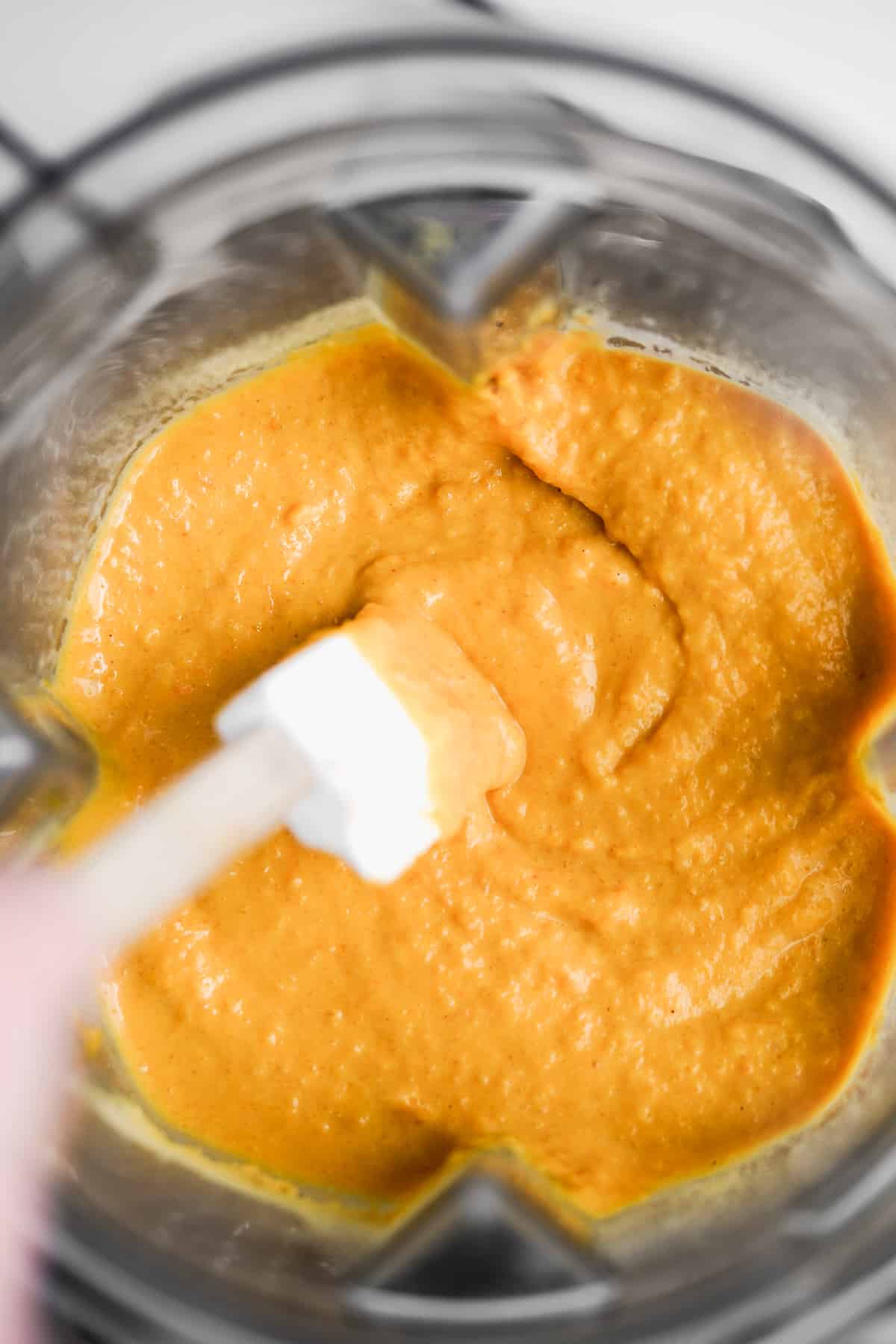 Overhead view of cheese sauce in a blender with a spatula.