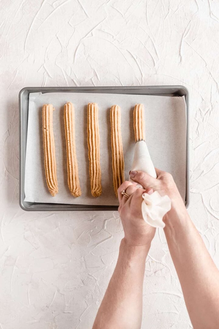 Person pipping dough onto a baking sheet to bake churros.