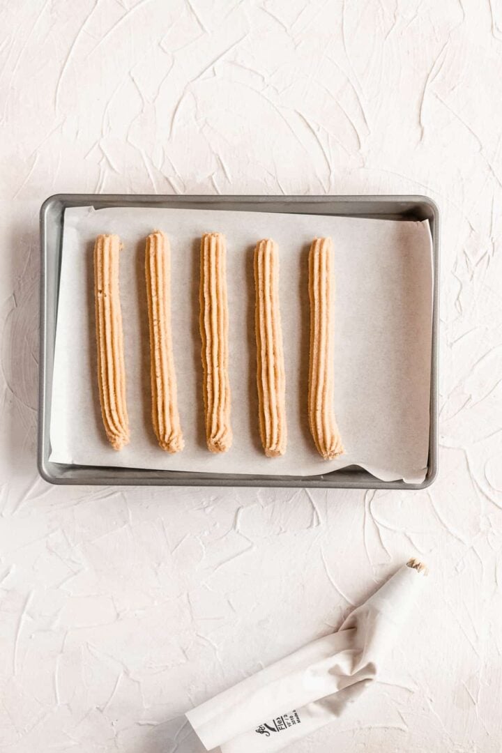 Gluten free churros on a baking sheet with parchment paper.