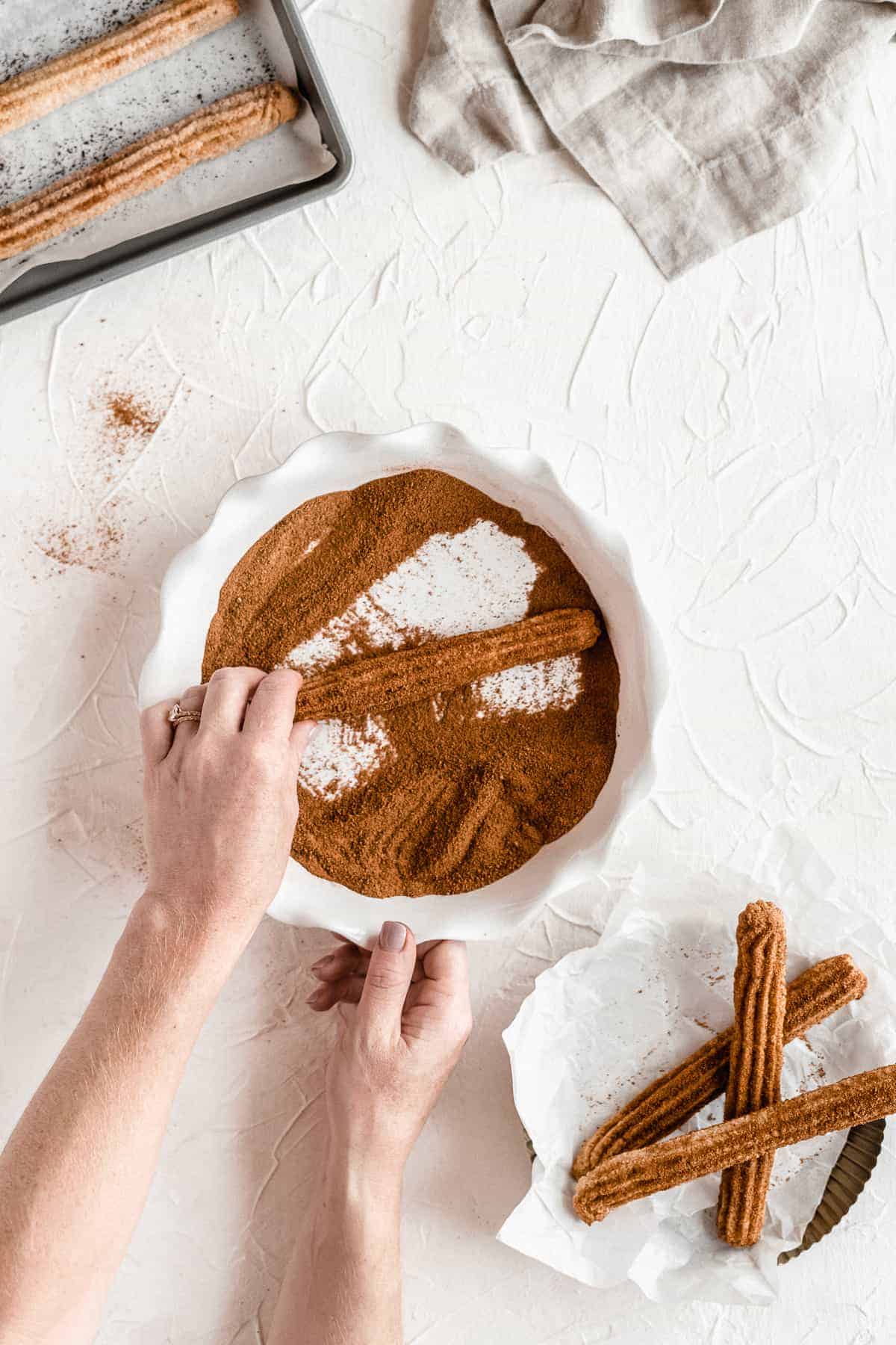 Person rolling vegan churro in cinnamon coating.