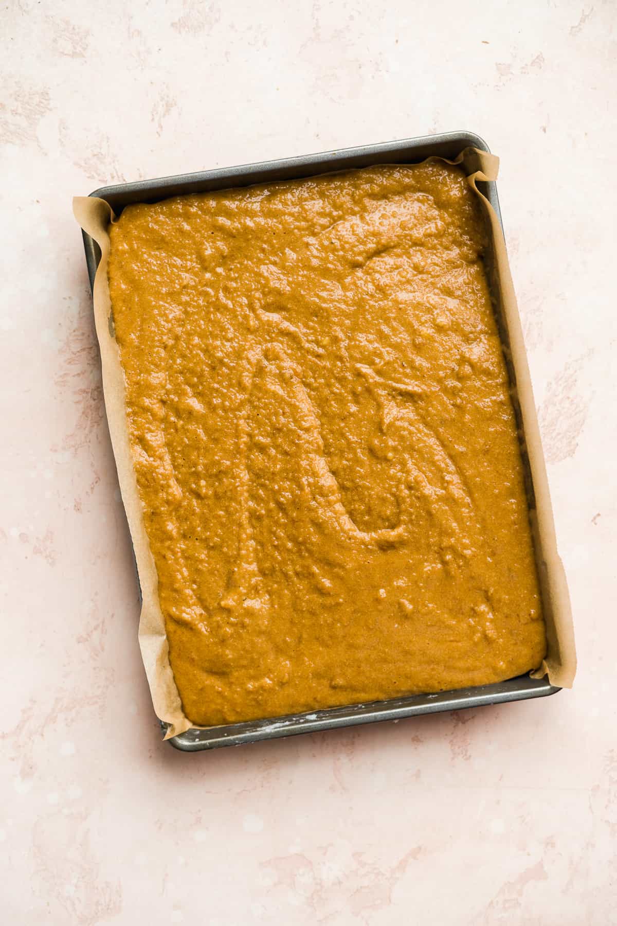 Tan cake batter inside a baking pan with parchment paper.