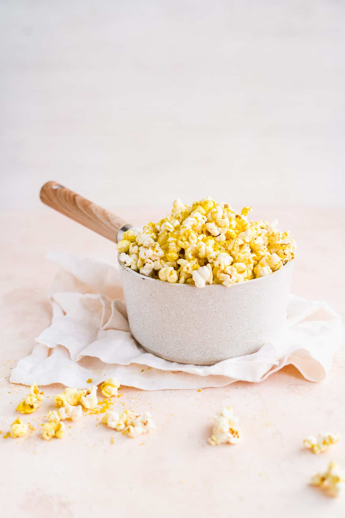 Grey pot overflowing with cheesy popcorn sitting on white linen.