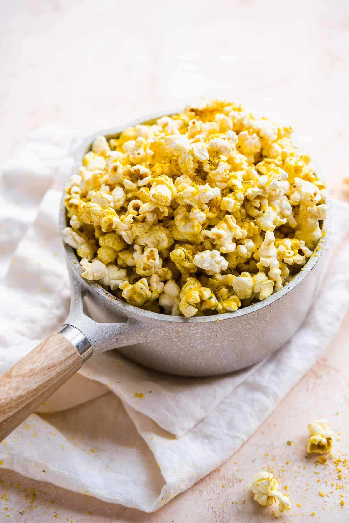 Grey pot filled with cheesy popcorn on white towel.