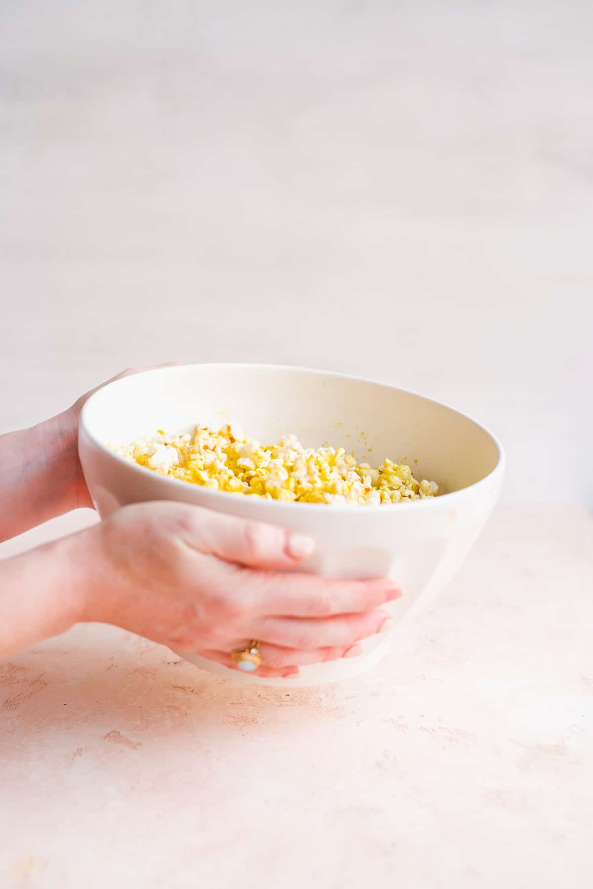 Two hands shaking white bowl with popcorn.