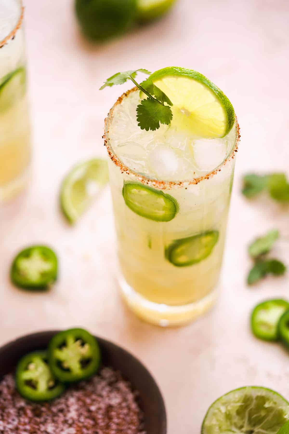 Tall salted cocktail glass filled with a lime green margarita and a lime wedge and cilantro stem on top.