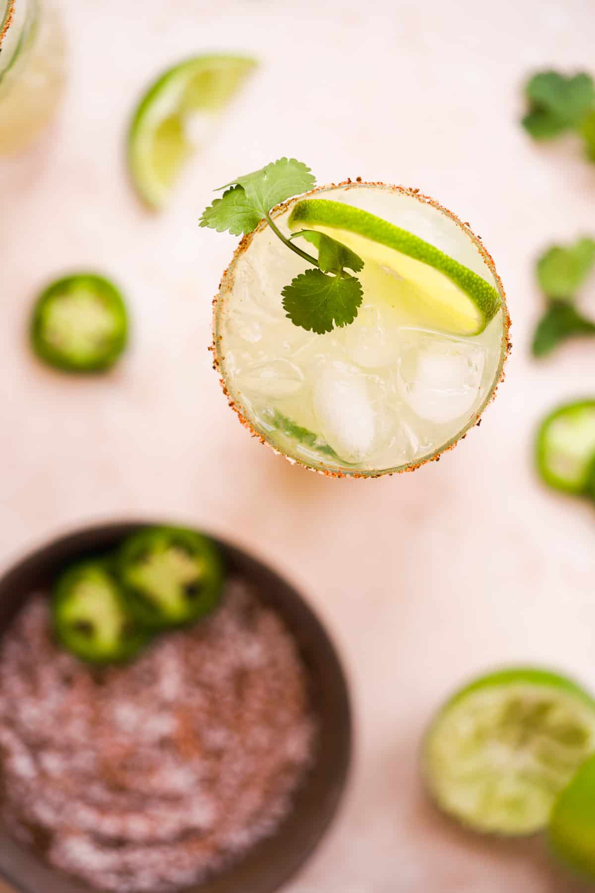 Overhead view of a cocktail glass with a lime wedge and cilantro stem inside.