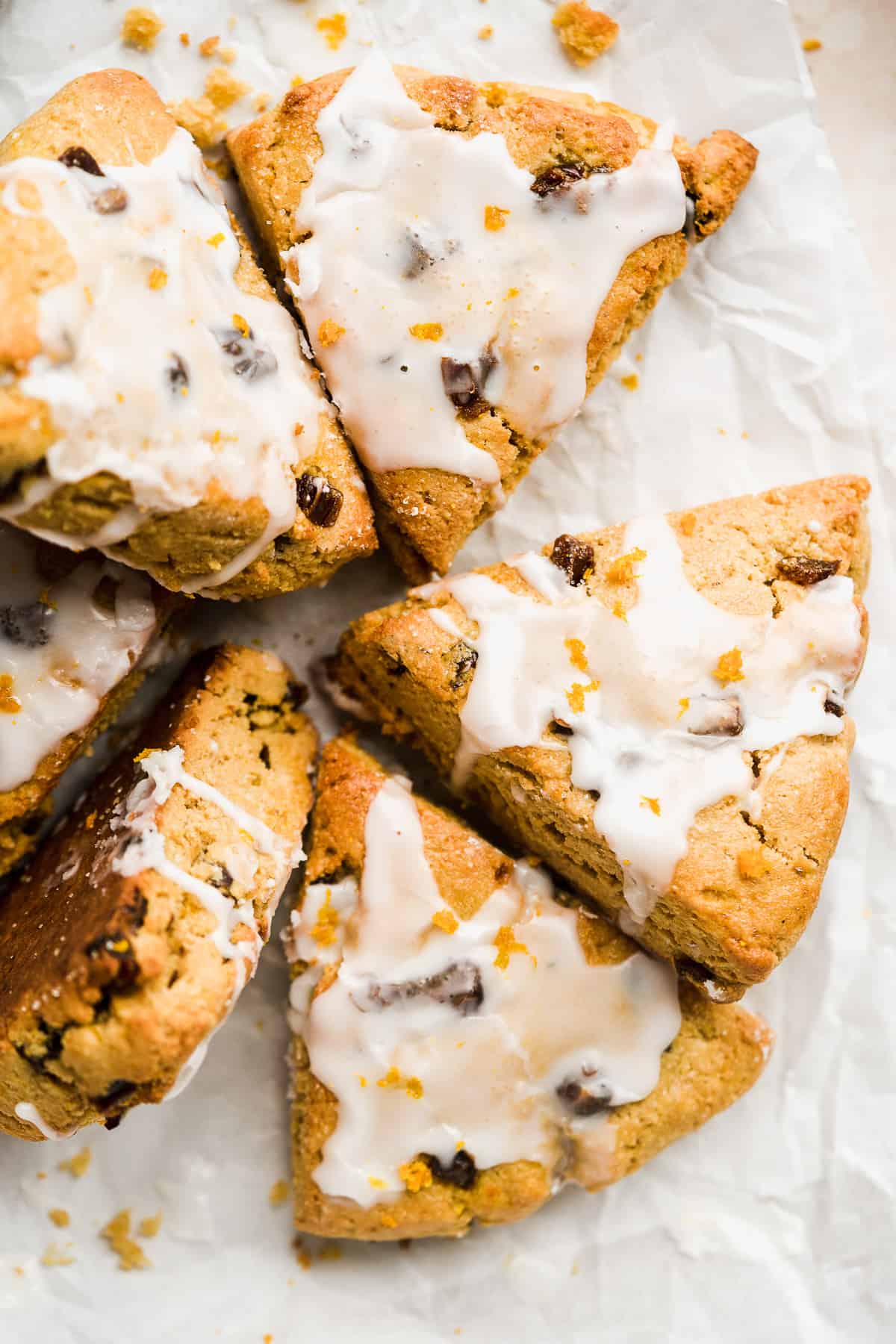 Golden triangular scones with white icing scattered on parchment paper.