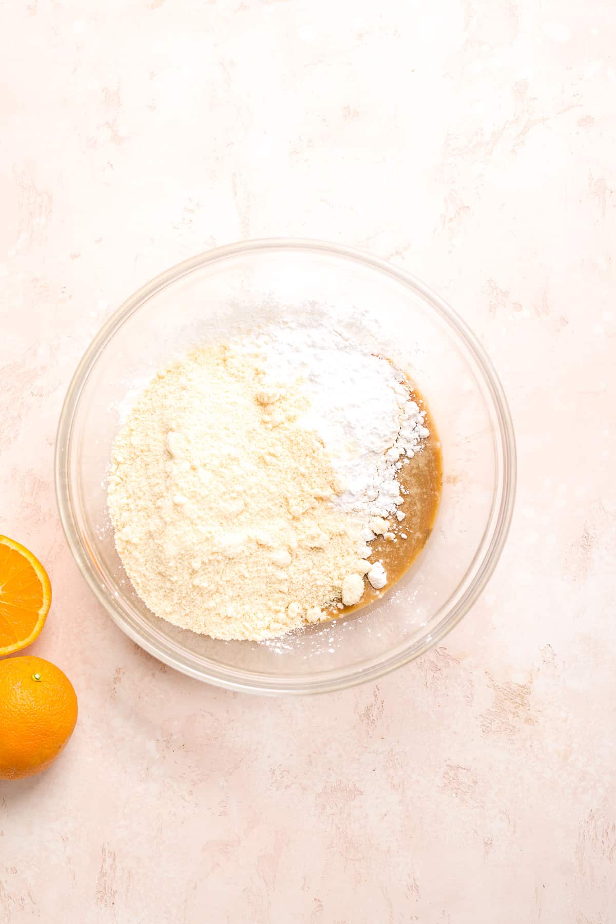 Large glass bowl with flour on top of tax mixture with orange off to the side.