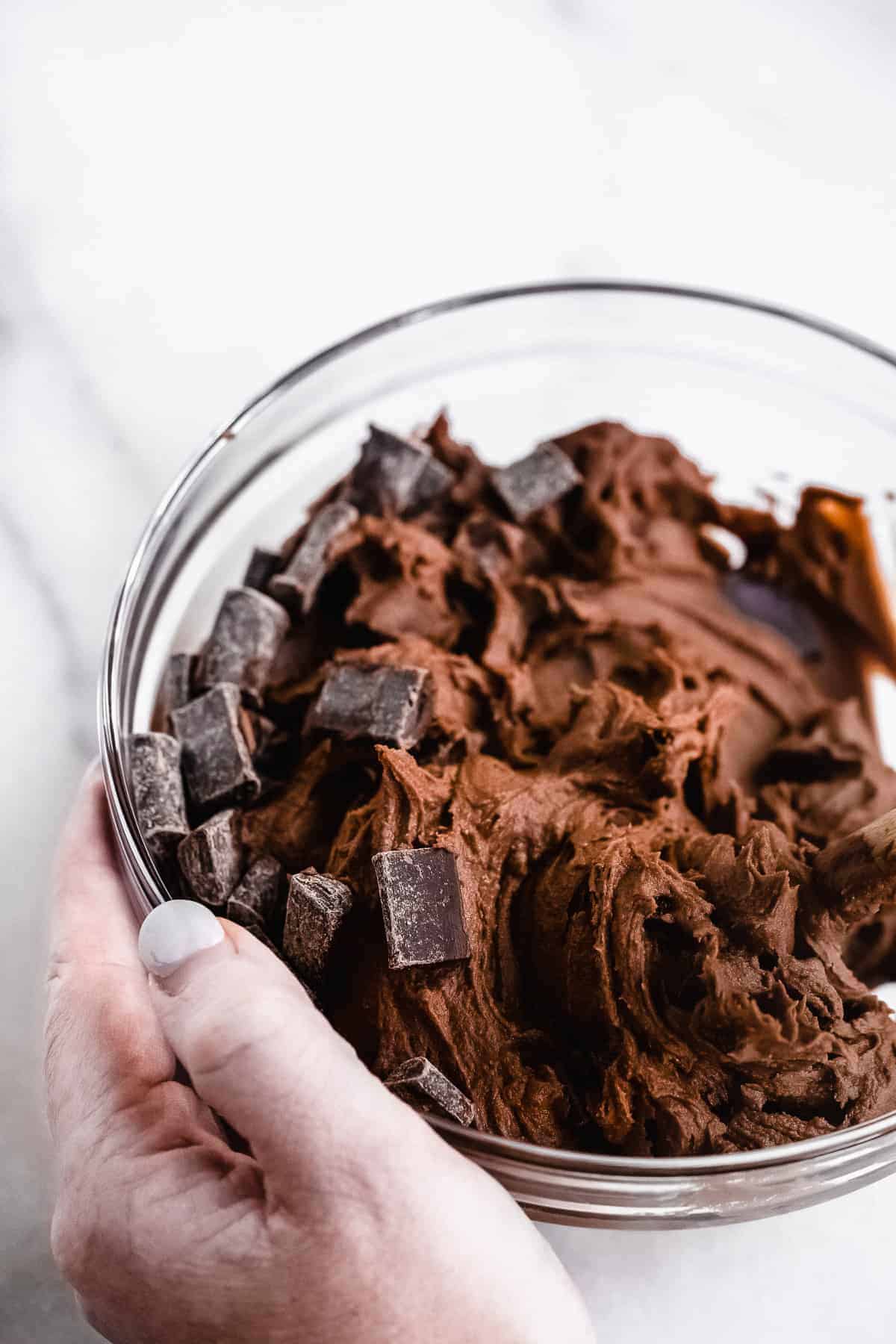 Glass bowl with edible brownie batter and chocolate chunks being mixed in.