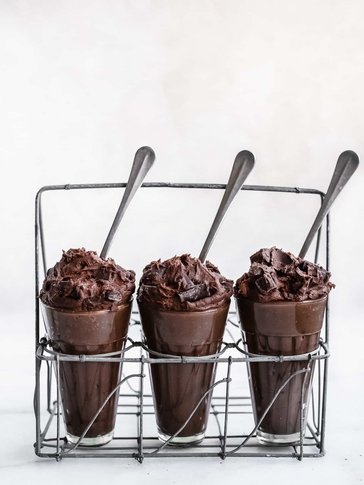 Three glasses overflowing with edible brownie batter with spoons stuck inside.