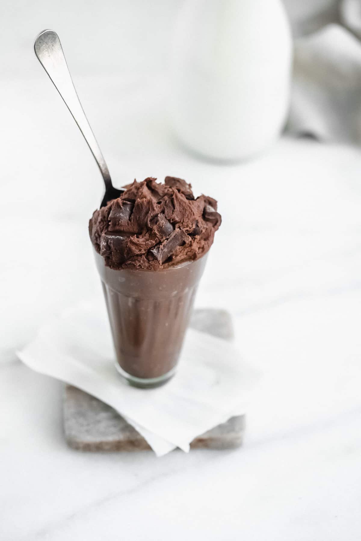 Glass full of edible brownie batter with chocolate chunks in the top and a spoon inside the glass.
