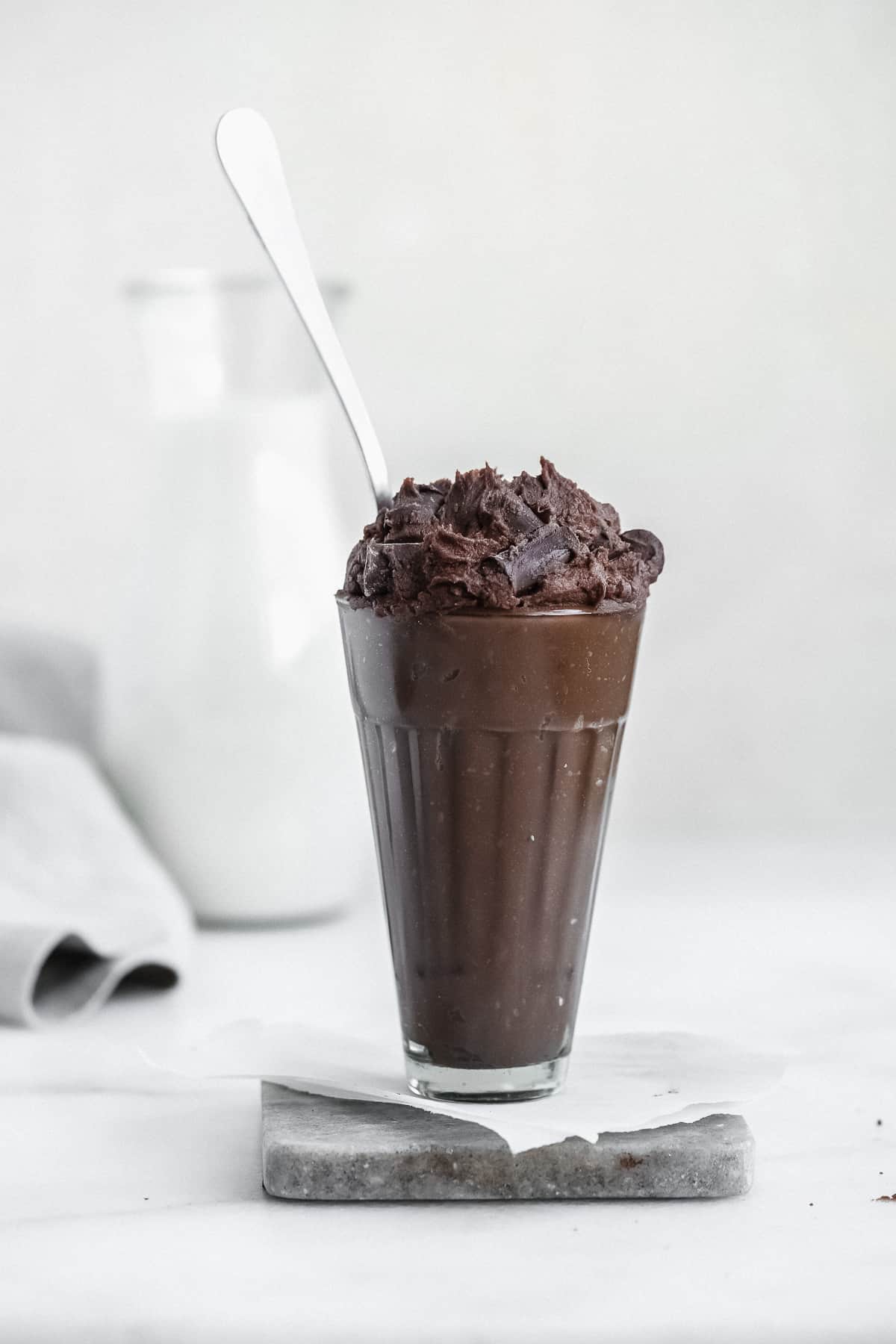 Glass with edible brownie batter on a marble coaster and a spoon sticking inside.