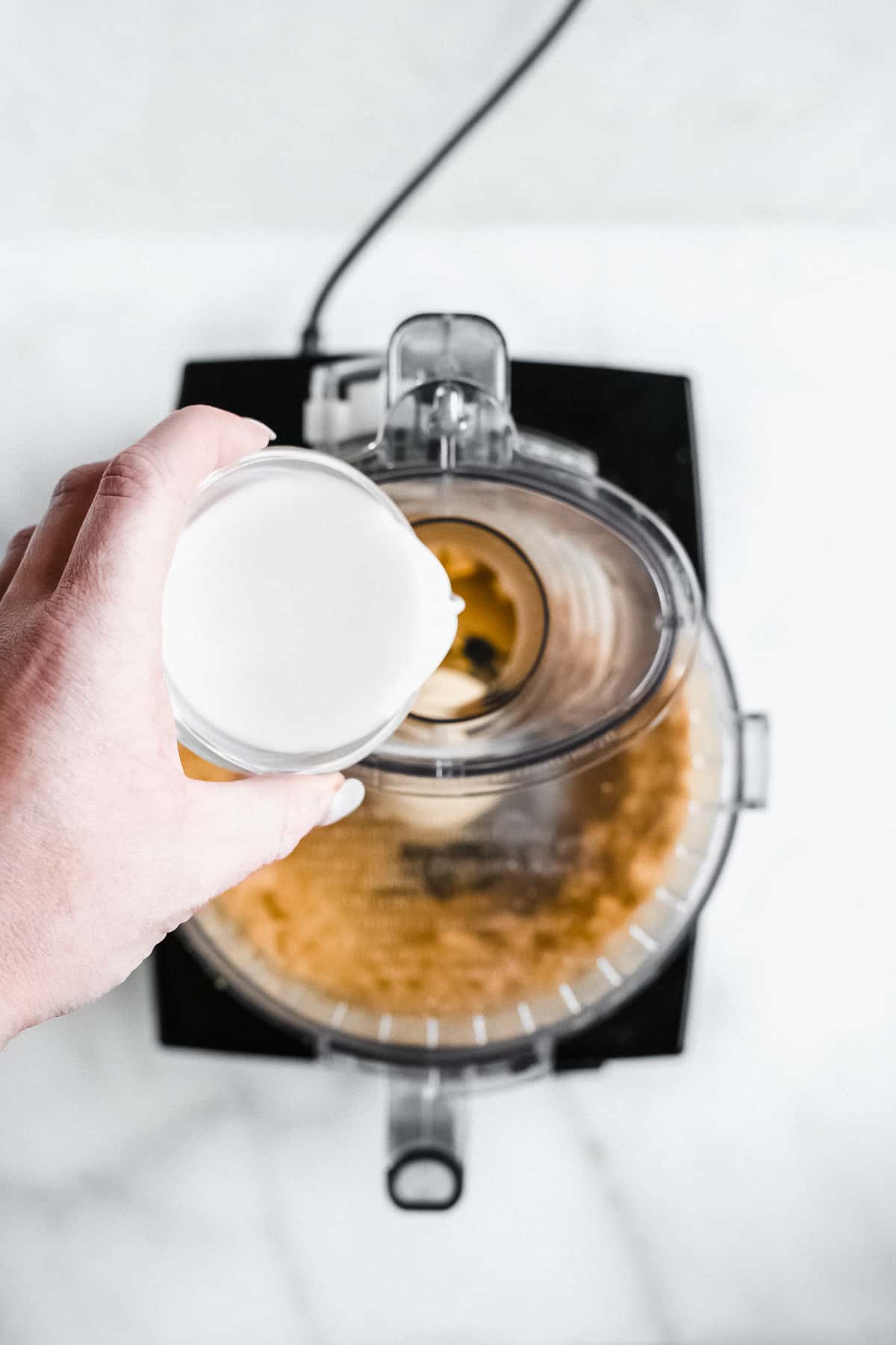 Person pouring milk into a food processor. 