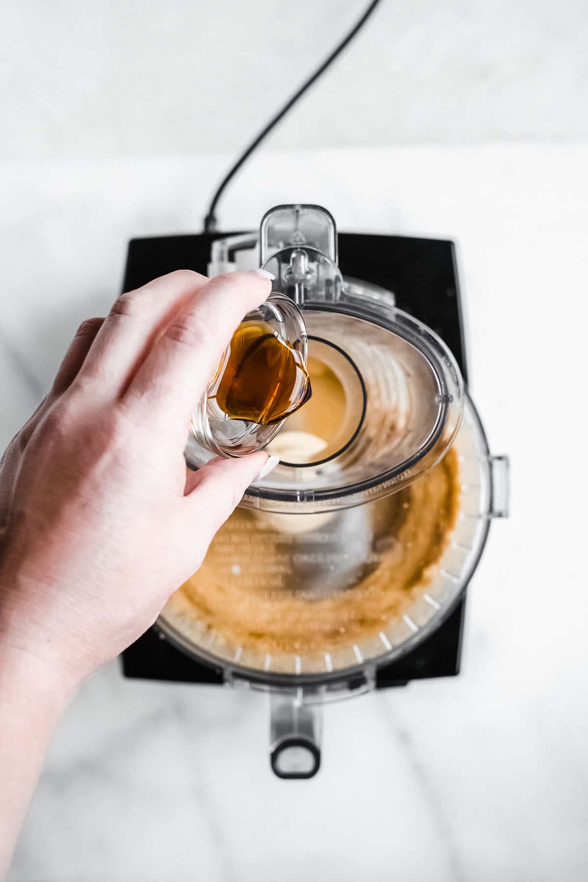 Person pouring vanilla into a food processor.
