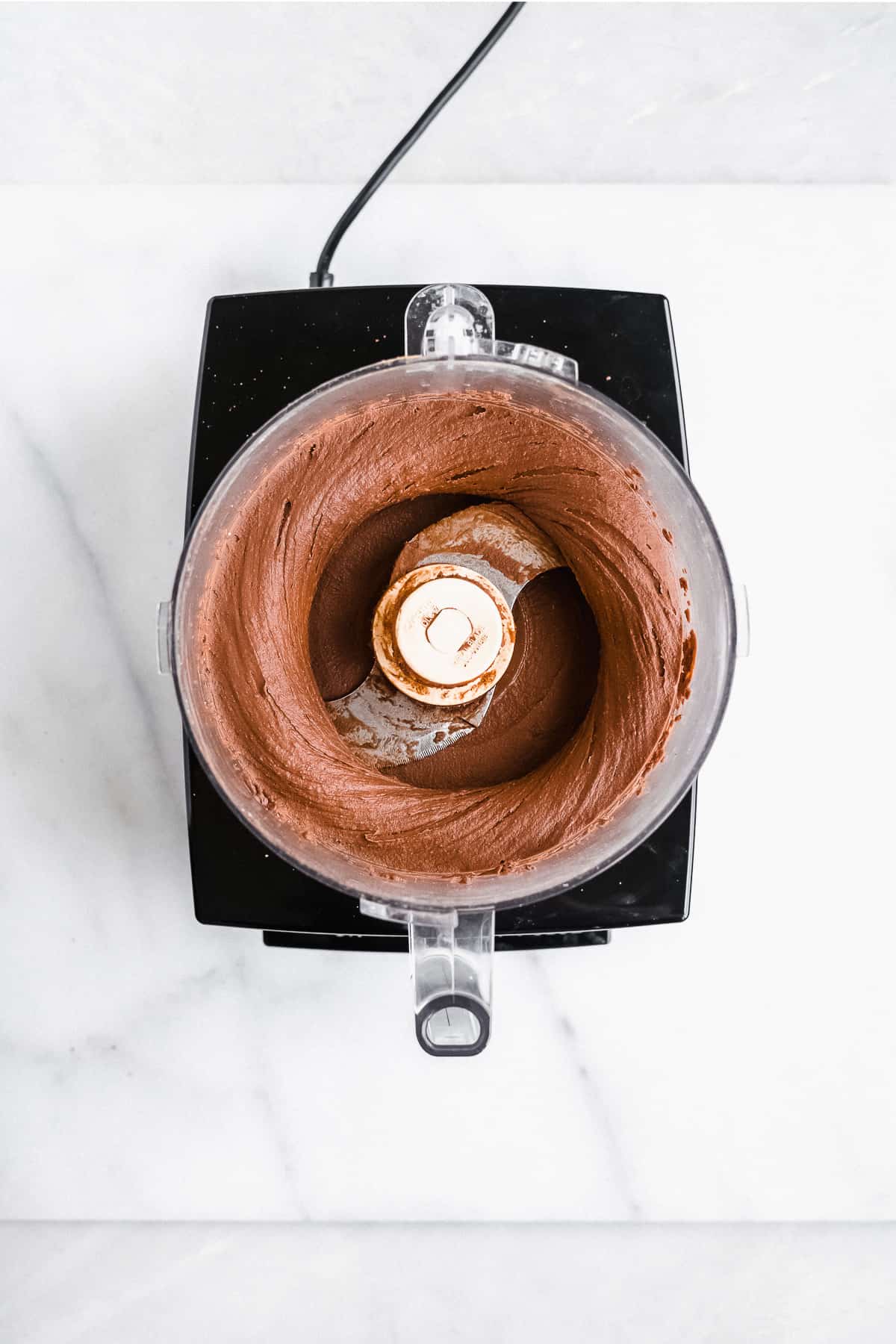 Inside view of food processor with edible brownie batter mixed inside.